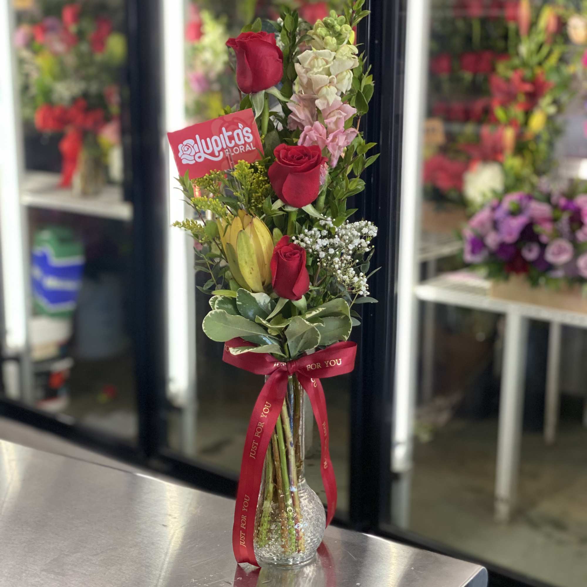 Tall bouquet of red roses and mixed blooms in a glass vase with a red ribbon