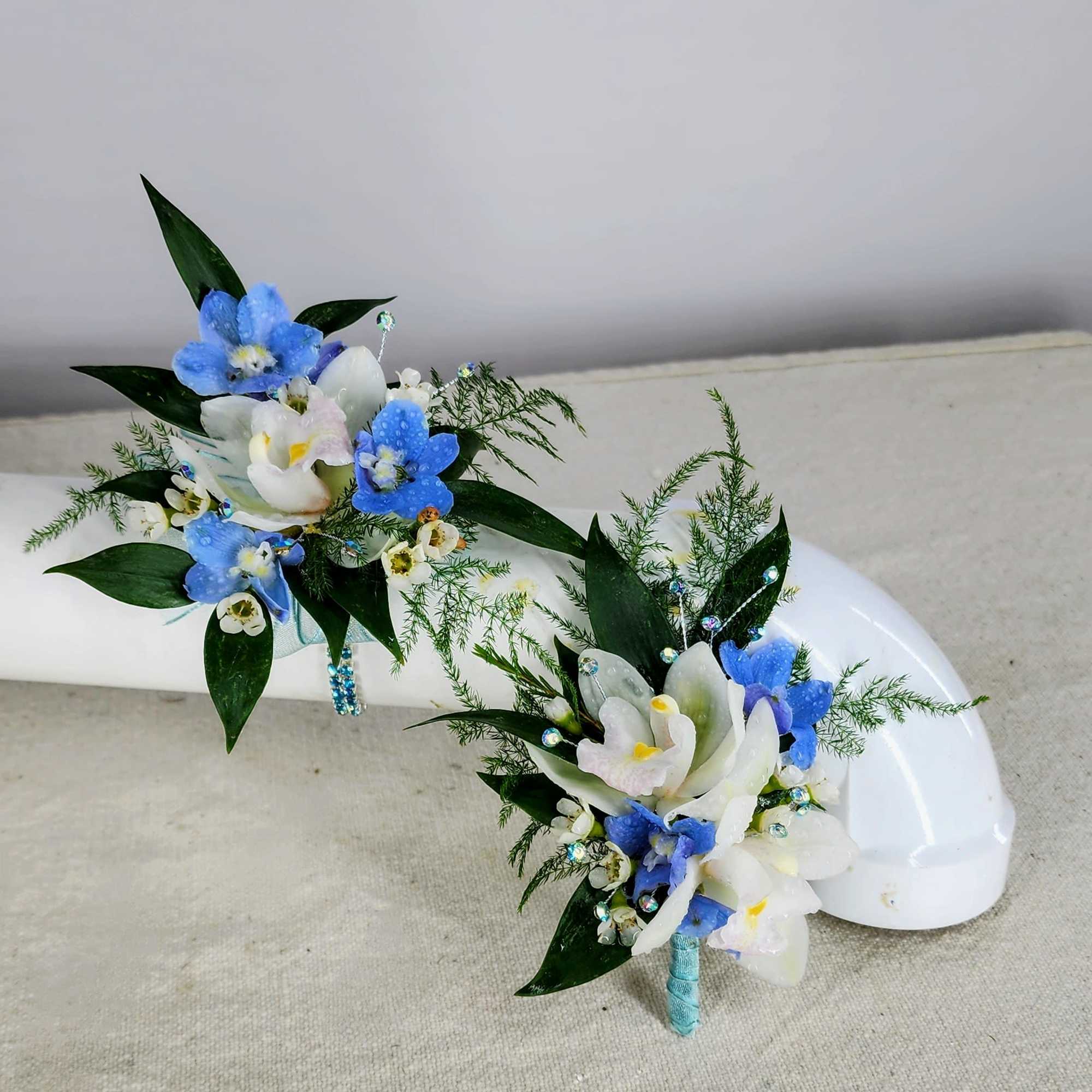 Two blue and white floral corsages with a white shell backdrop