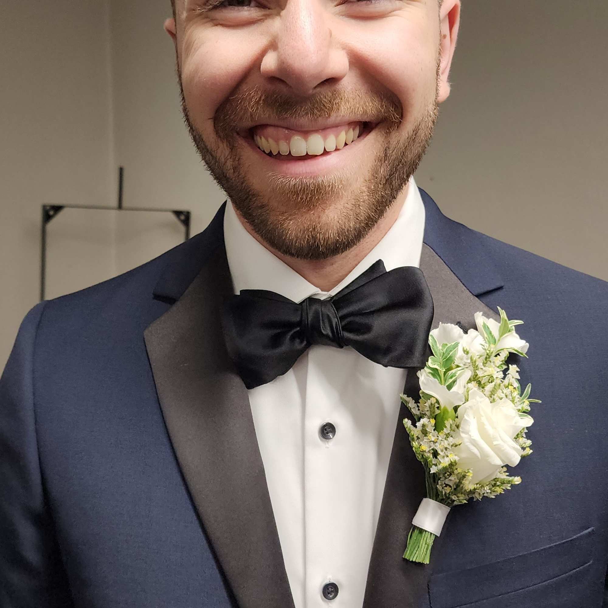 Smiling man in a tuxedo wearing a white boutonniere