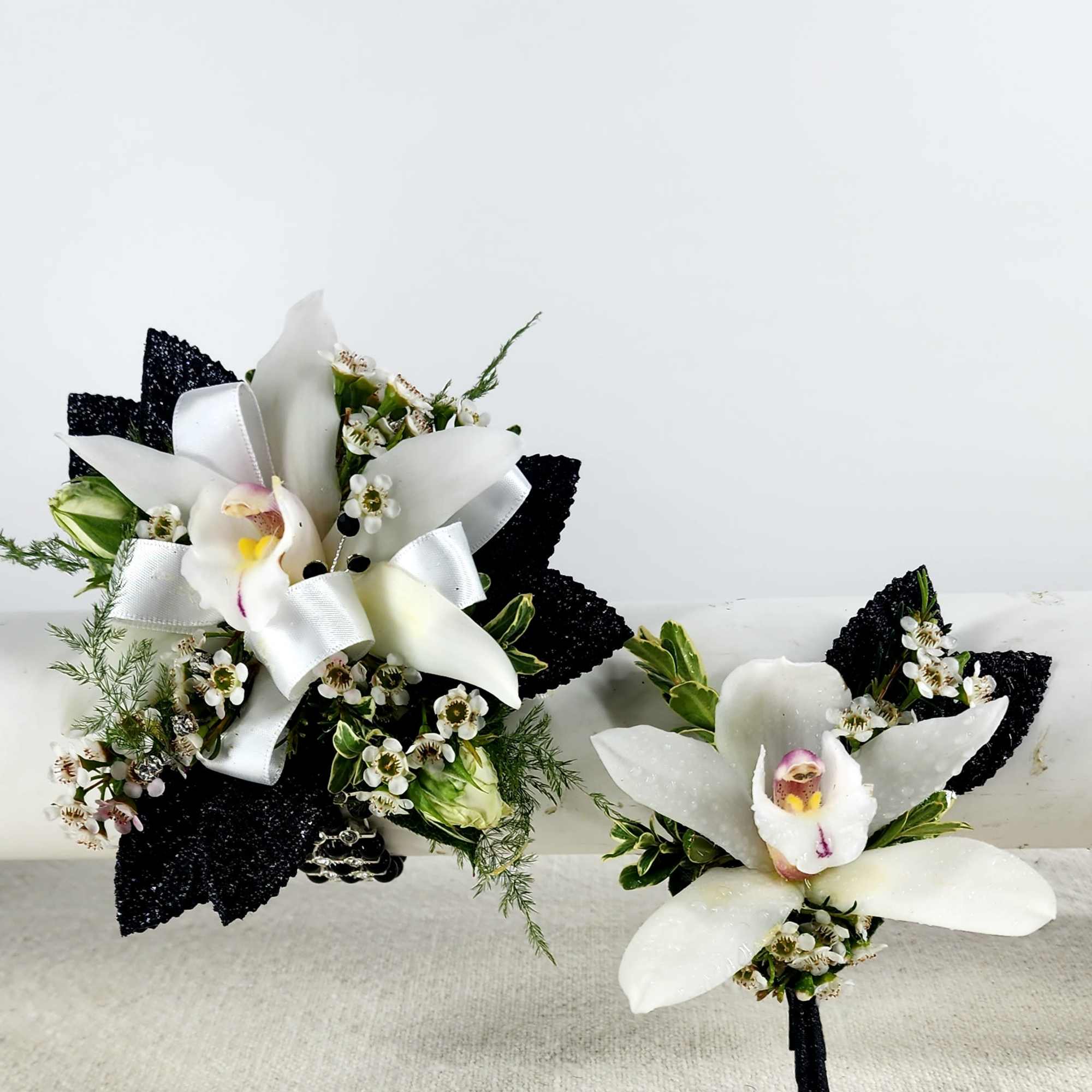 Two white orchid boutonnieres with black ribbon accents