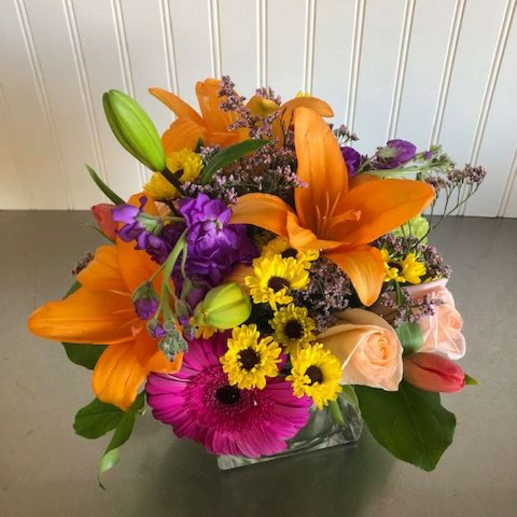 Bright mixed bouquet with orange lilies, purple flowers, and yellow daisies in a glass vase