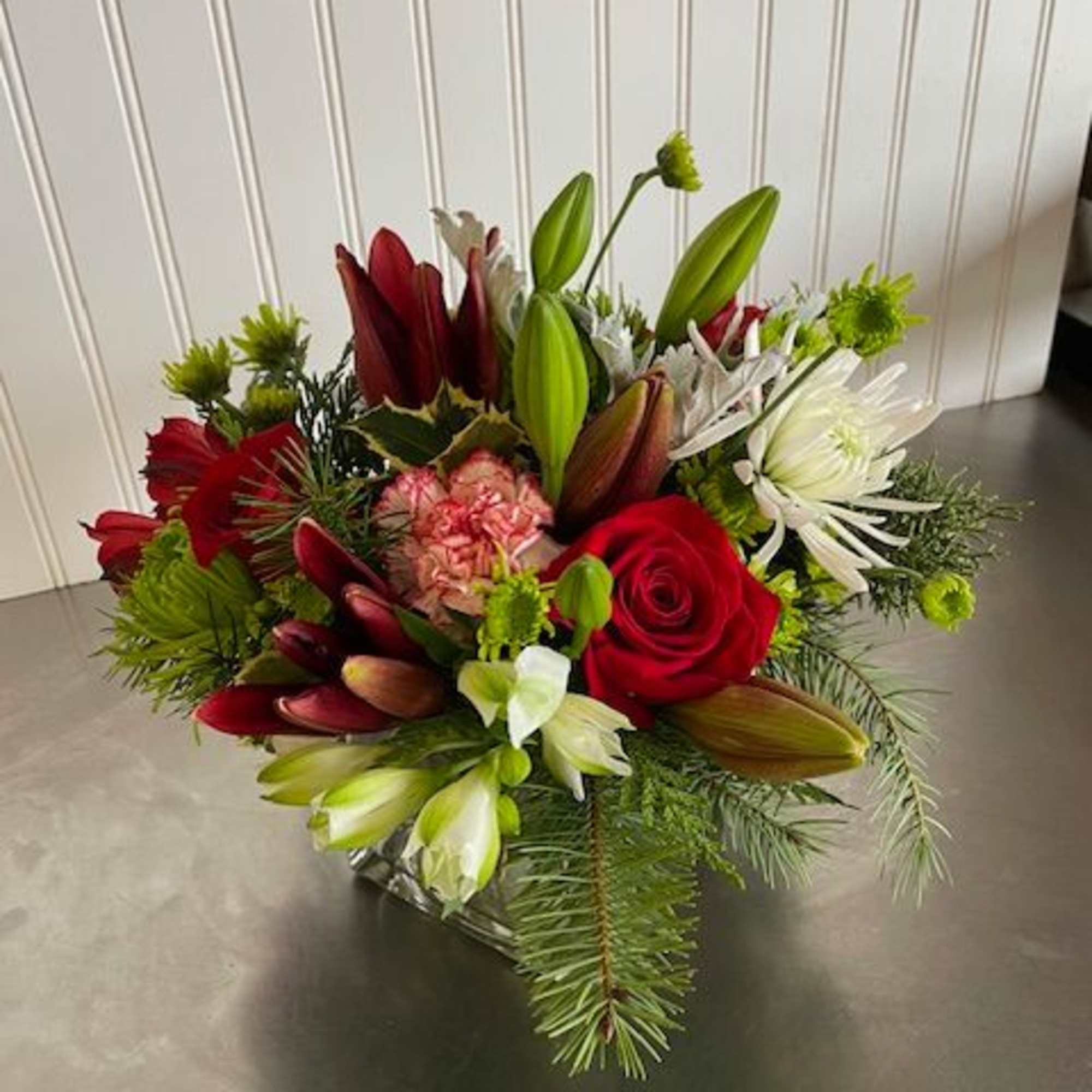 Mixed bouquet of red roses, lilies, and white blooms in a low container