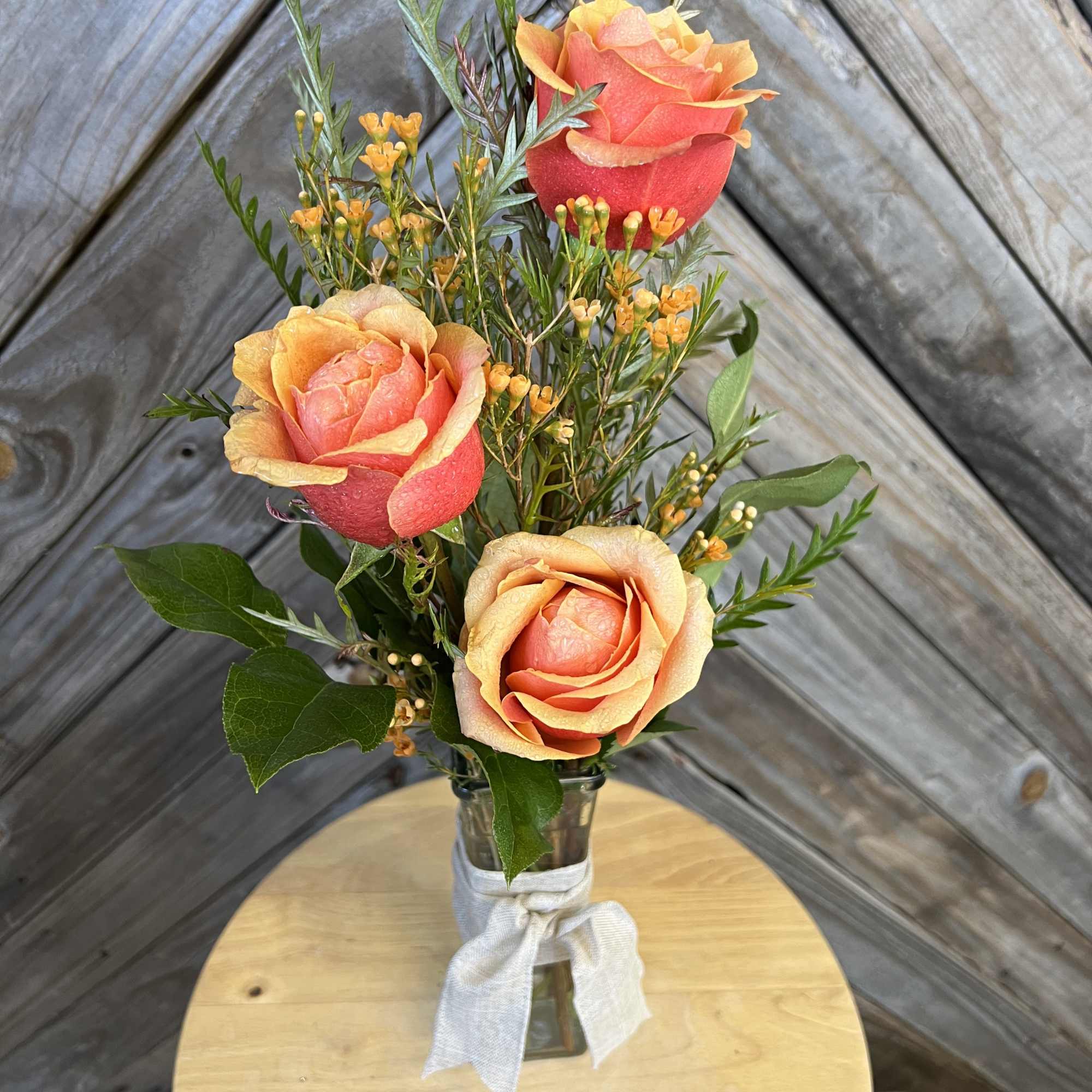 Three coral roses in a small glass vase with a white ribbon