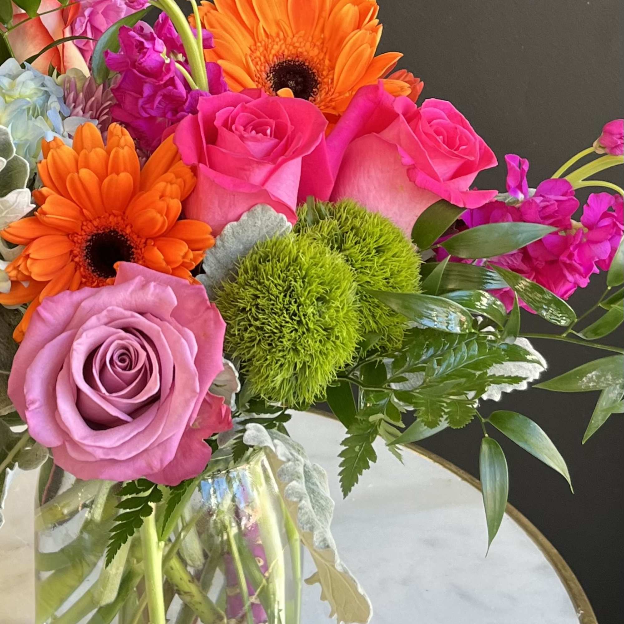 Pink roses and orange gerbera daisies in a clear glass vase