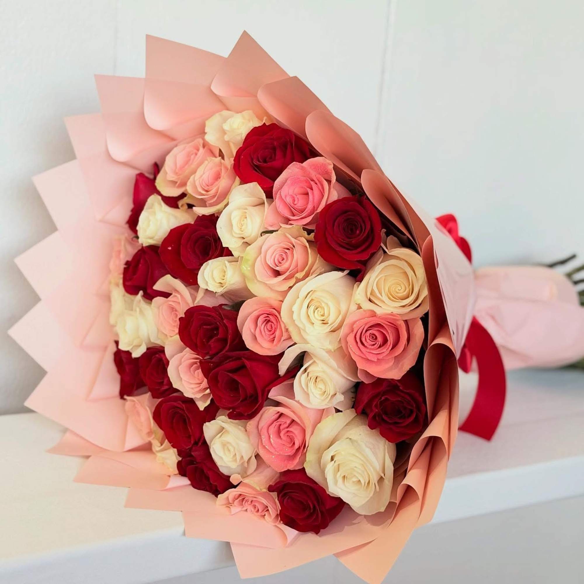 Bouquet of red, pink, and cream roses wrapped in pale pink paper