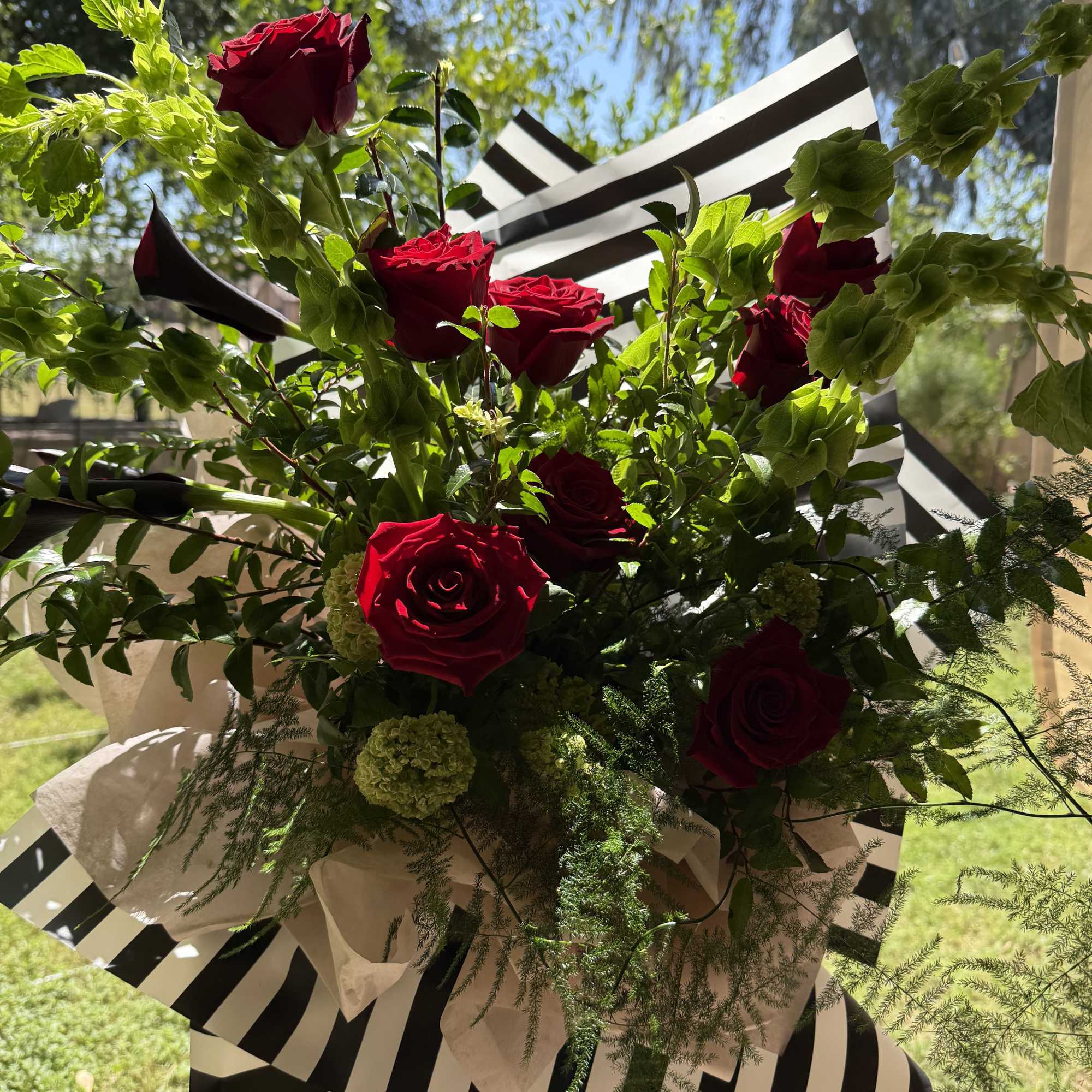 Deep, velvety red roses arranged with airy greenery and mini calla lilies