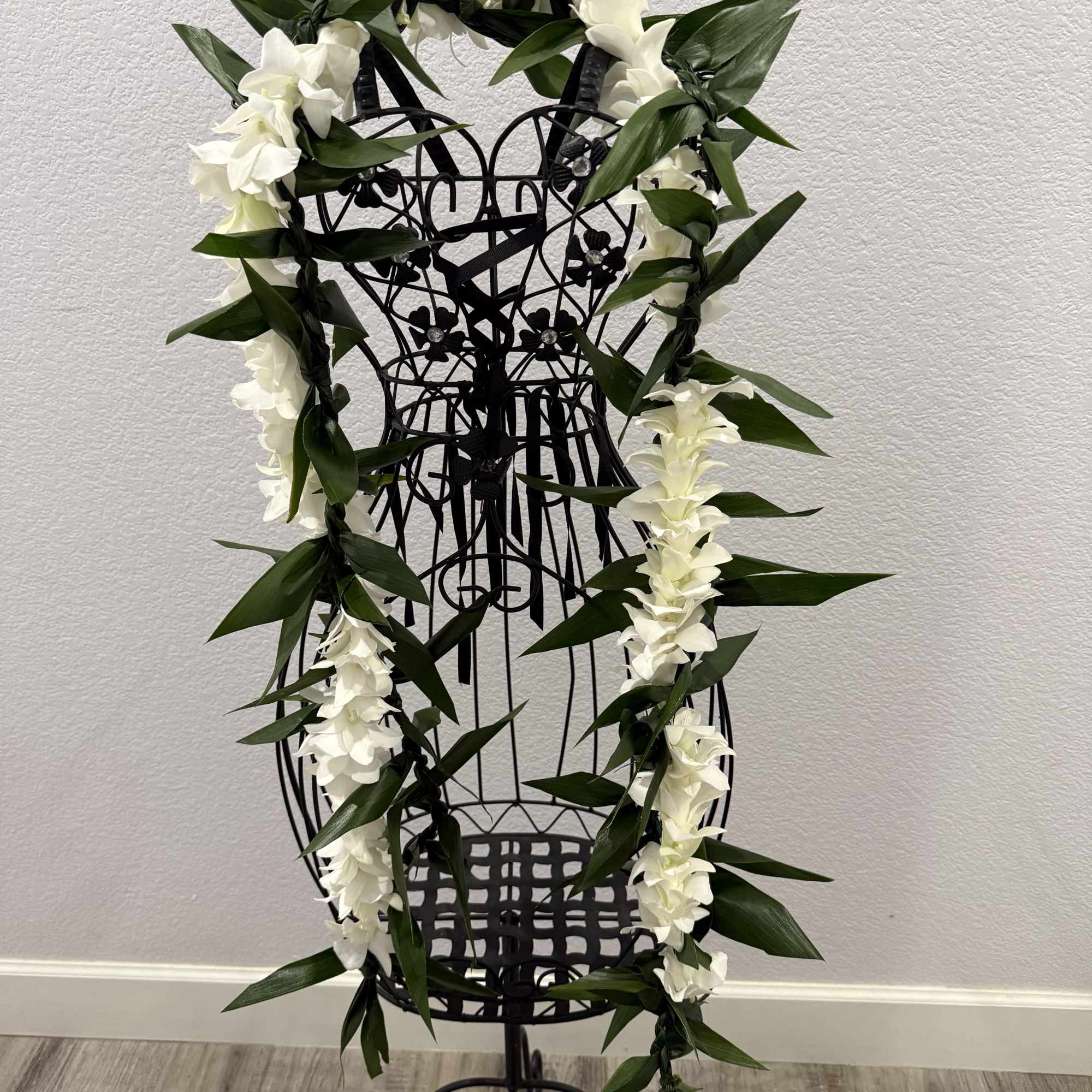 A long white orchid and ti leaf lei draped in a vertical