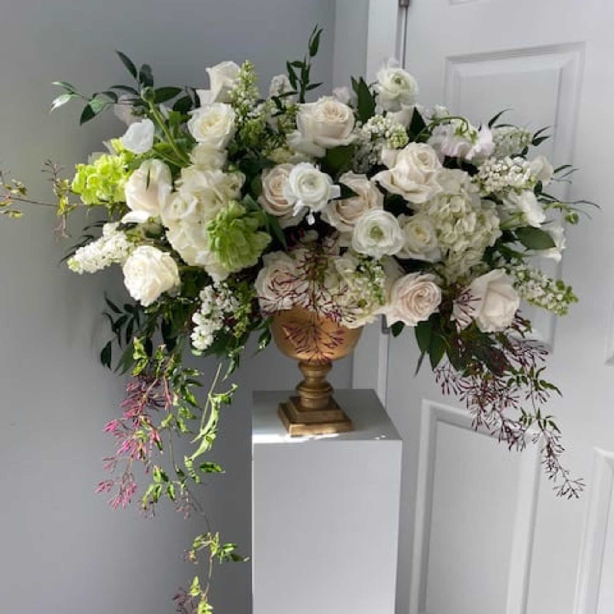 White rose arrangement in a gold urn with trailing greenery