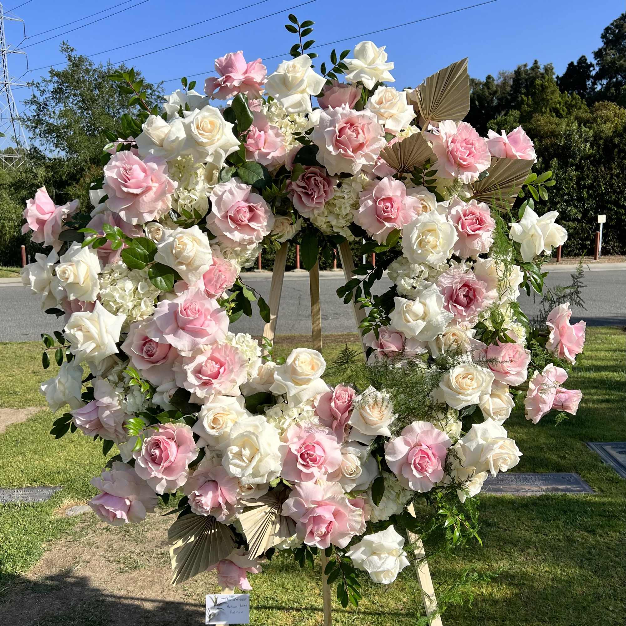 Large pink and white rose wreath on a wooden stand outdoors