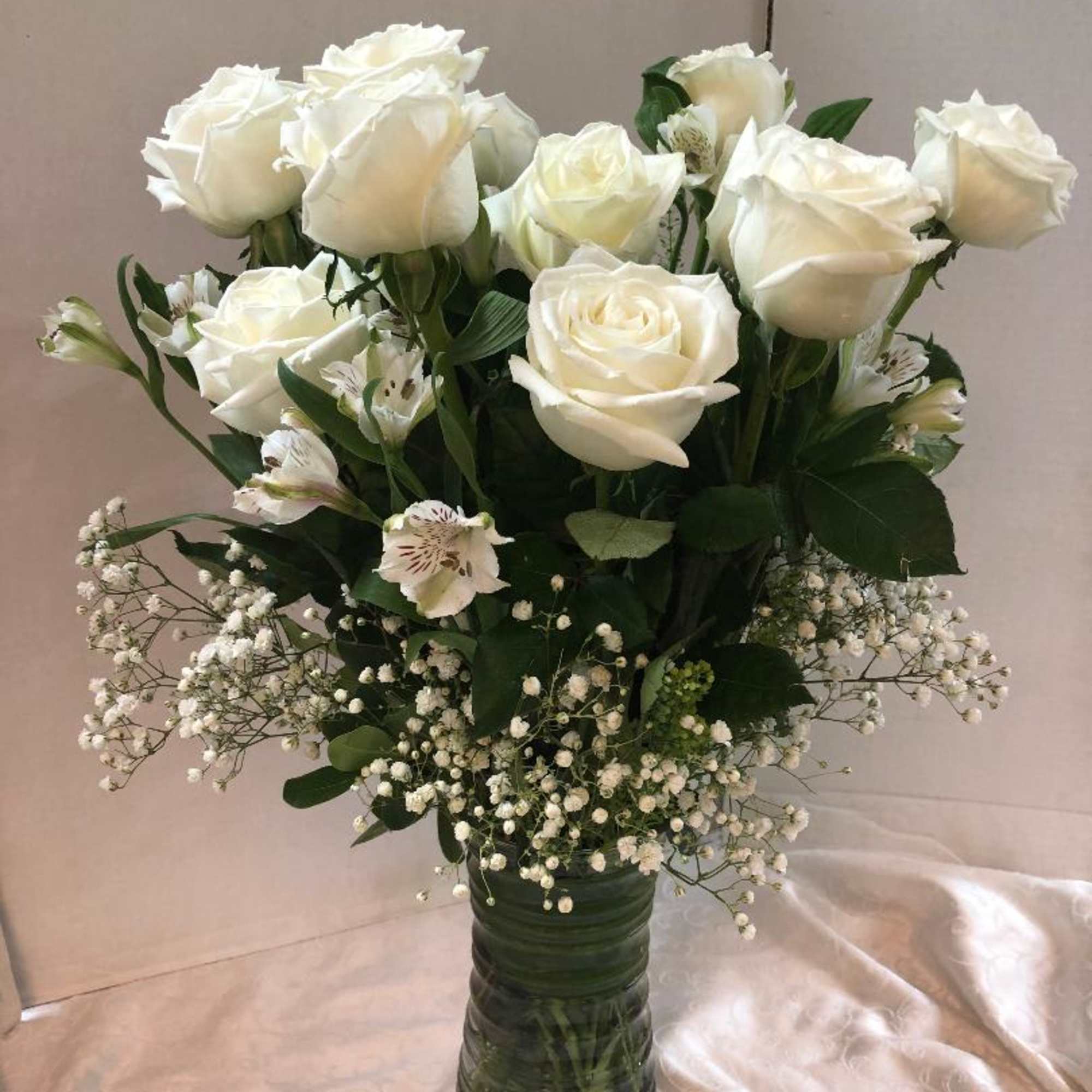 White roses and small white filler flowers in a tall glass vase