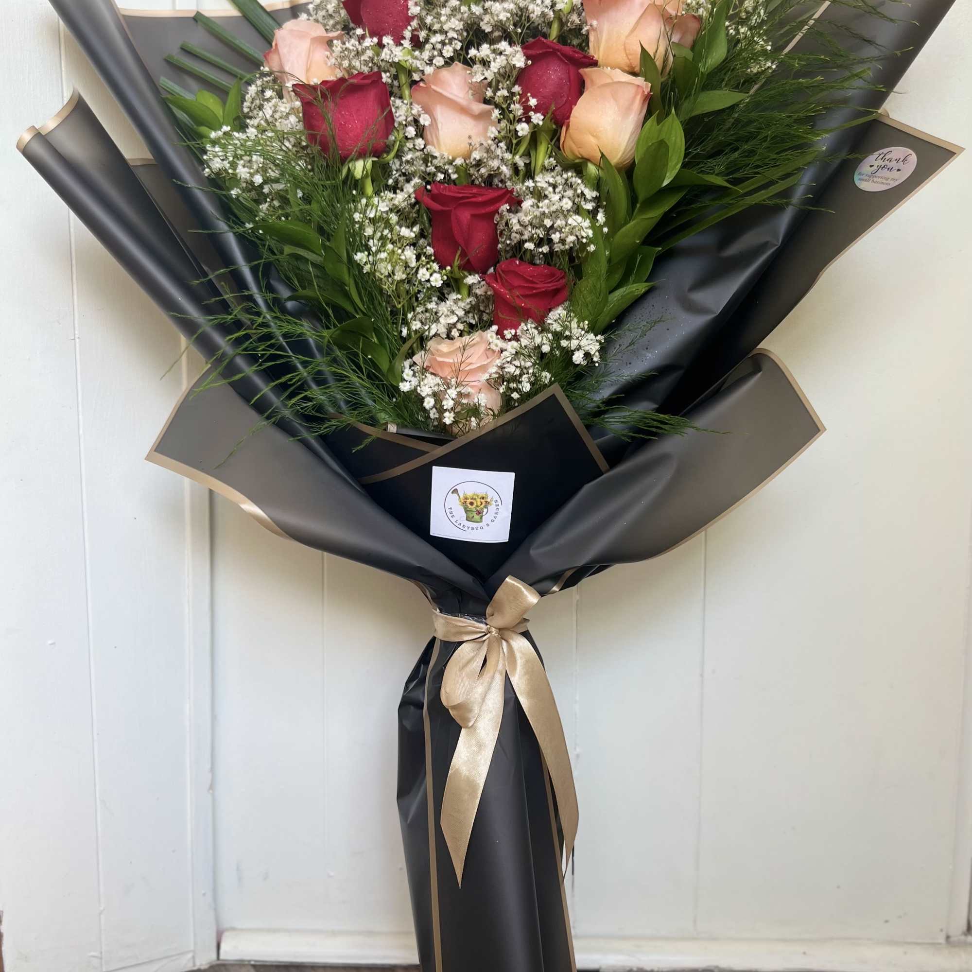 Bouquet of red and blush roses wrapped in black paper with a gold ribbon