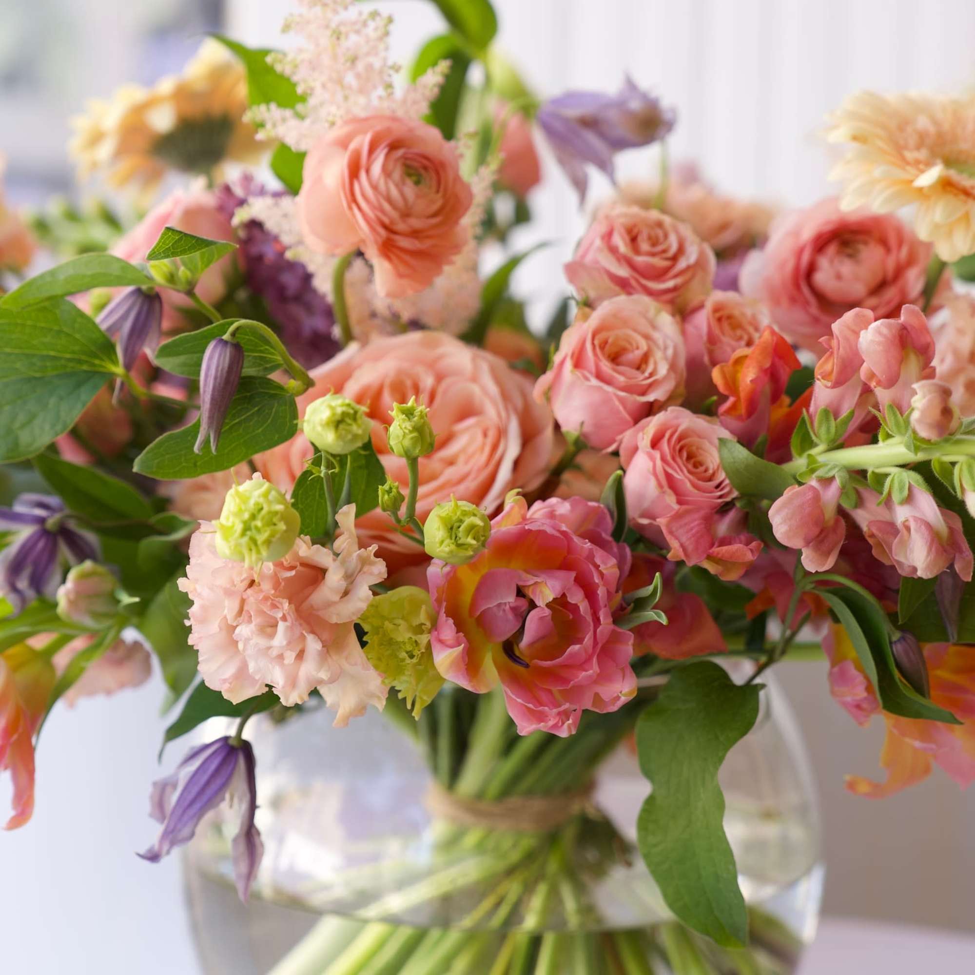 An airy, garden-style floral arrangement featuring peach garden roses, ranunculus, tulips, snapdragons
