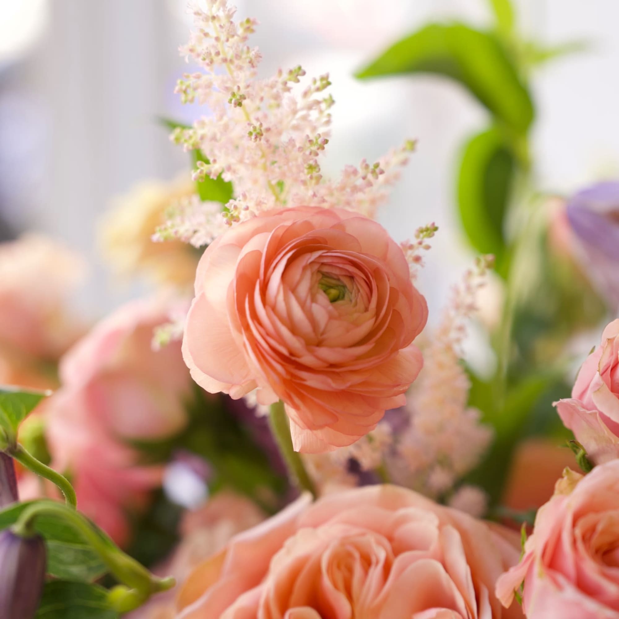 An airy, garden-style floral arrangement featuring peach garden roses, ranunculus, tulips, snapdragons