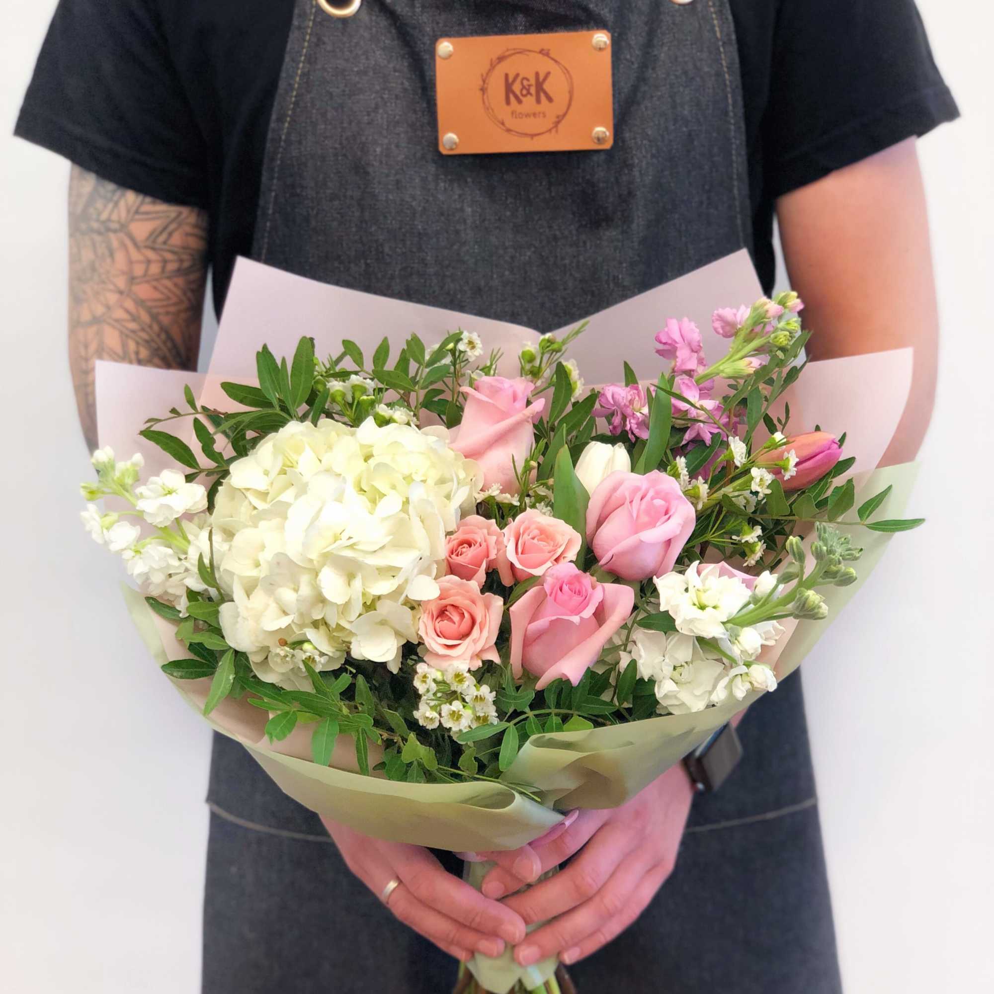 Handheld bouquet of pink and white flowers wrapped in pale paper