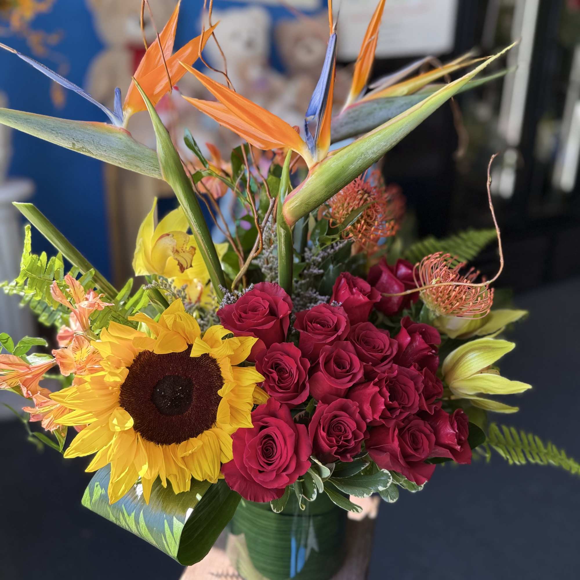 Tropical arrangement with birds of paradise, red roses, sunflower and lilies in a glass vase