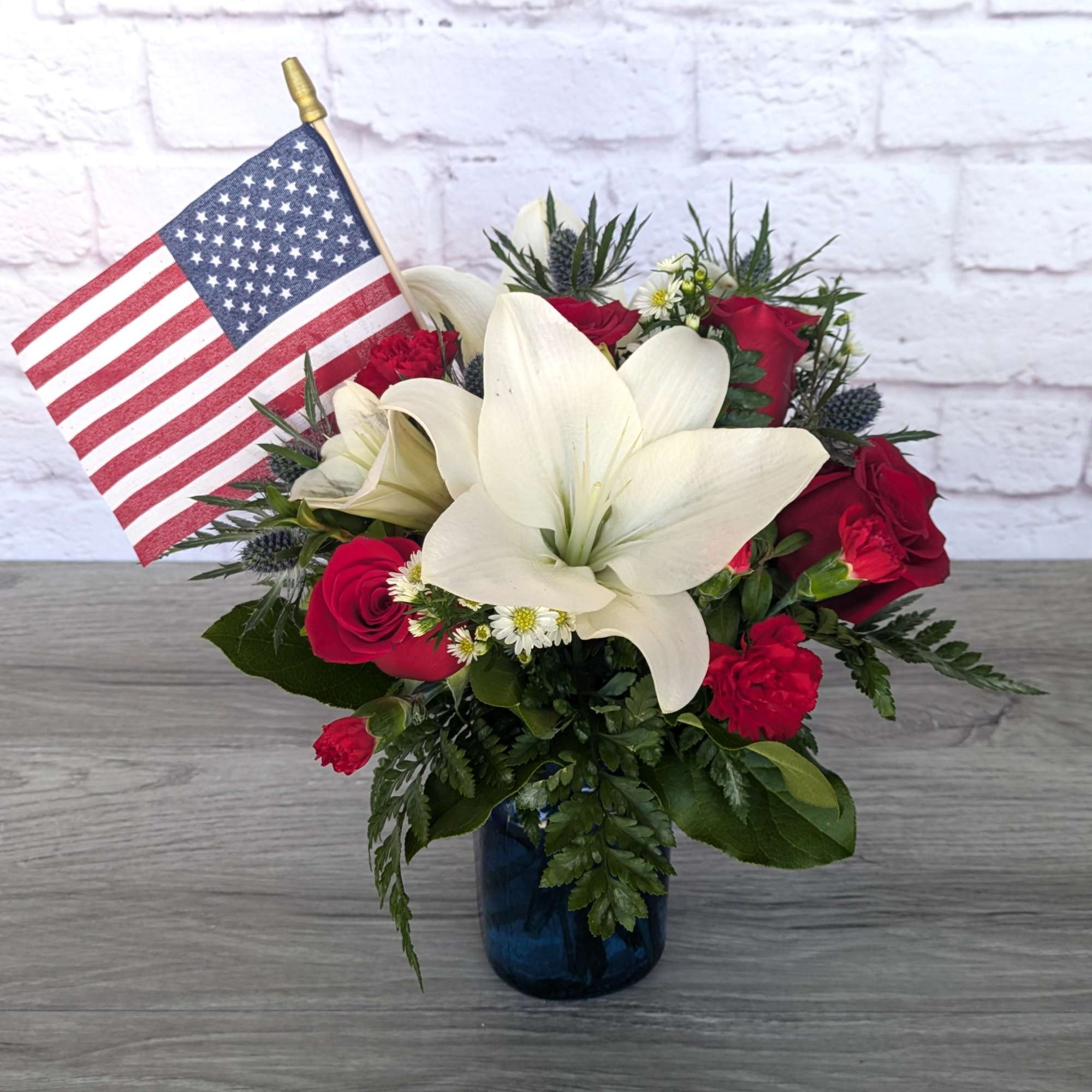 Red and white floral arrangement in a blue vase with an American flag