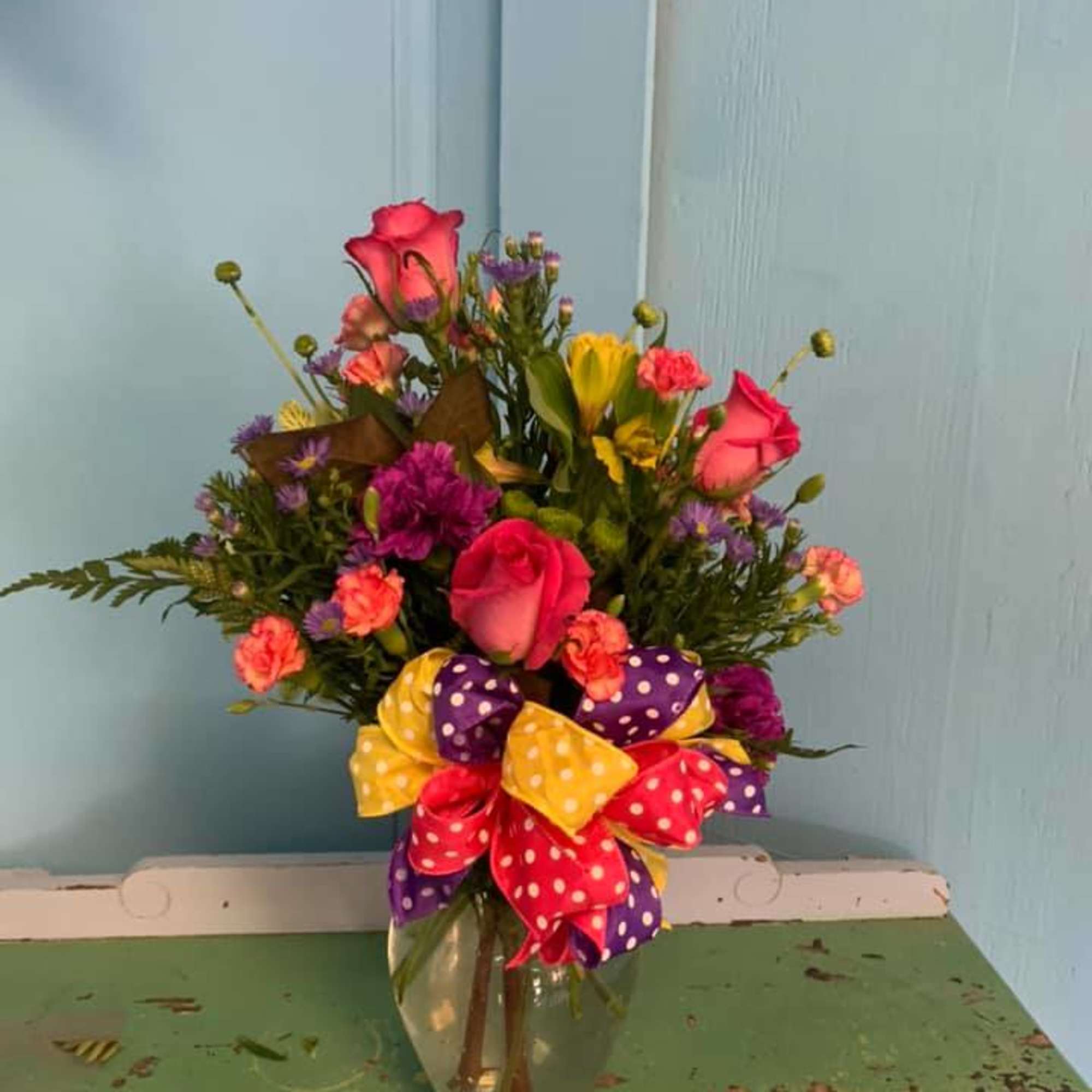 Mixed bouquet of pink, yellow, and purple flowers in a glass vase with a polka-dot bow