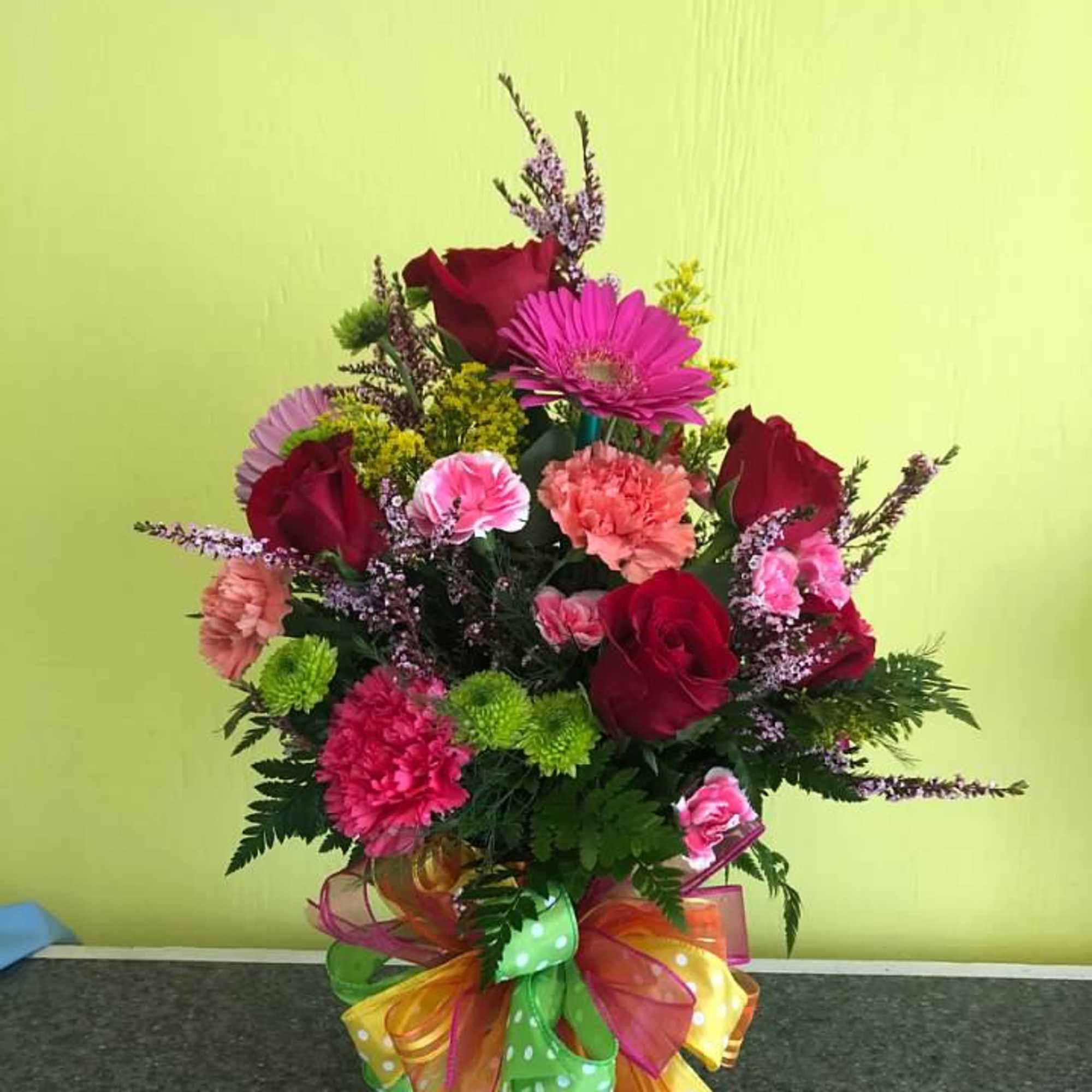 Mixed bouquet of red roses, pink carnations, and gerbera daisies in a glass vase