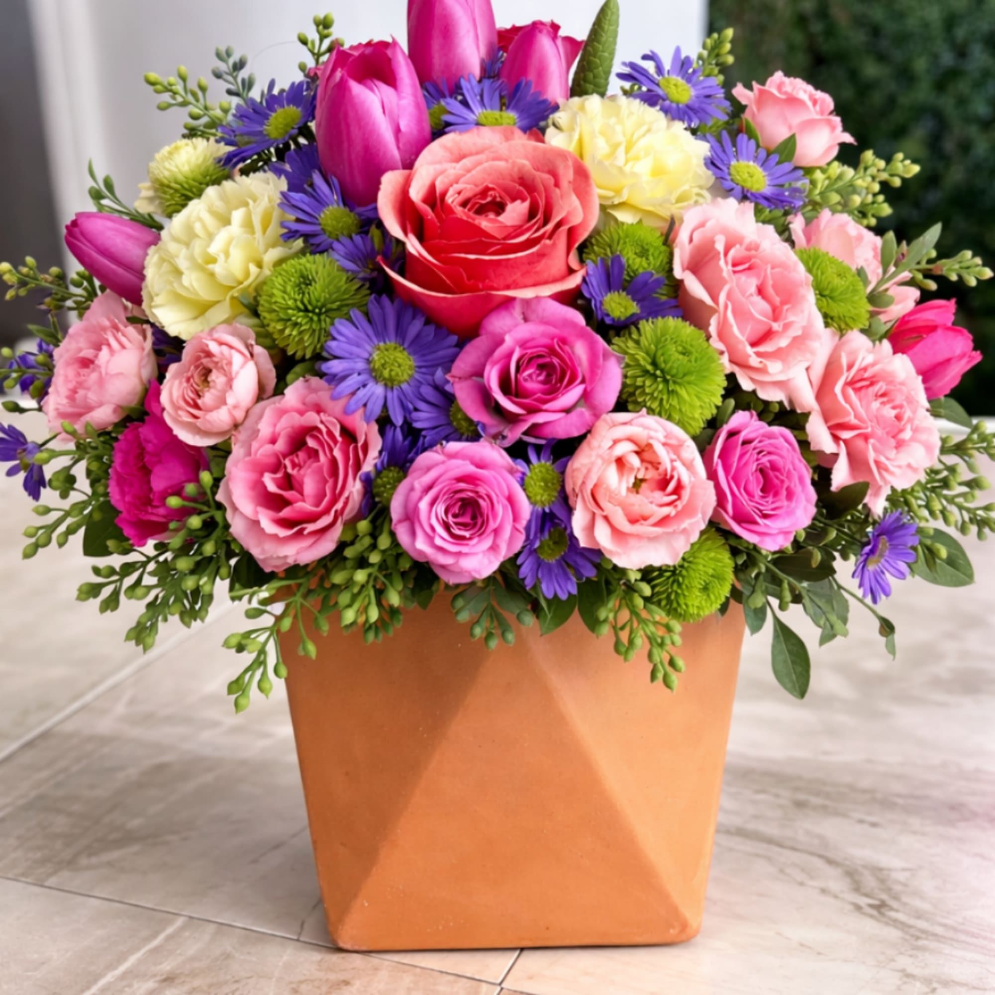 Bright mixed arrangement of pink roses, tulips, and purple asters in a terracotta pot