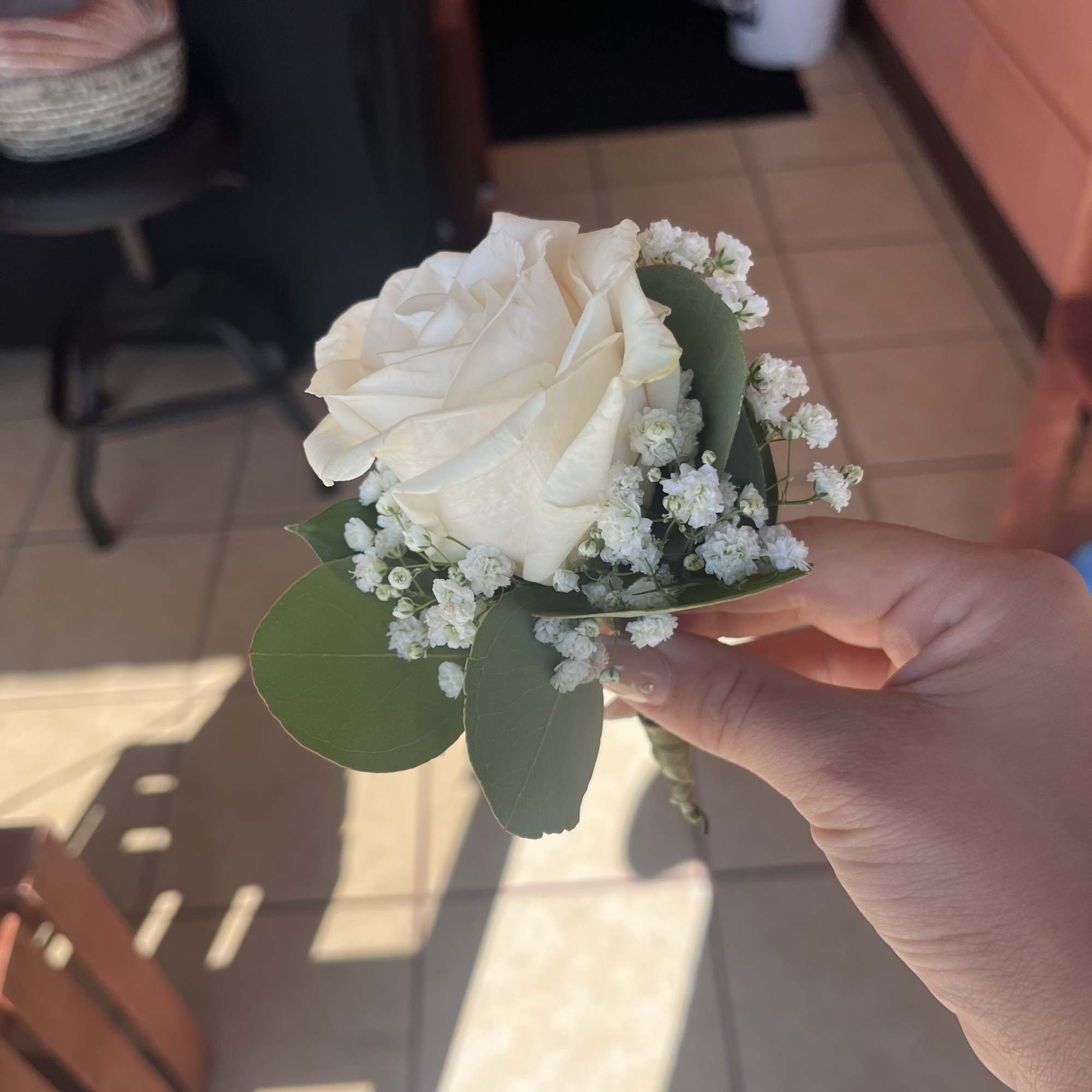 White rose boutonniere with baby's breath and green leaves
