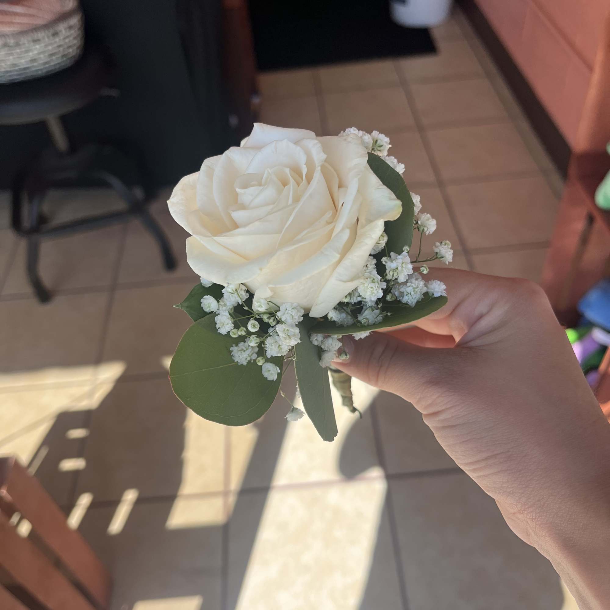 White rose boutonniere with baby's breath and green leaves