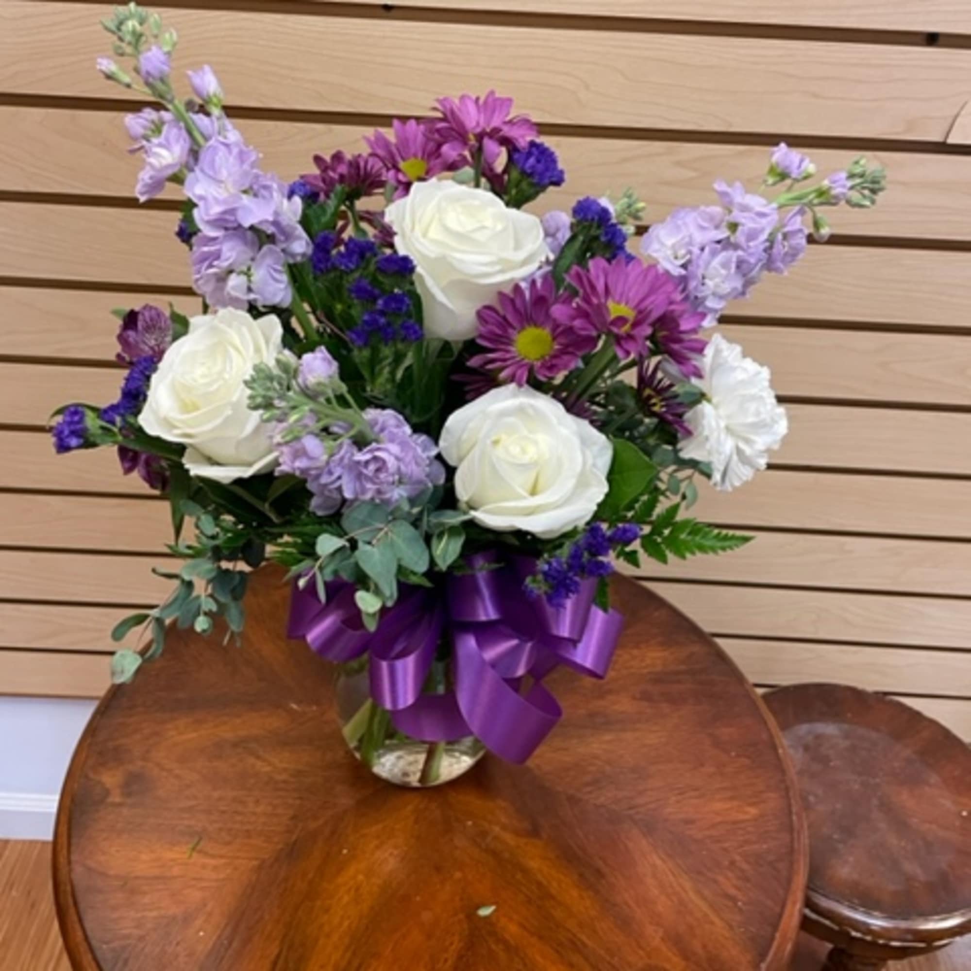 White roses and purple flowers in a glass vase with a purple ribbon