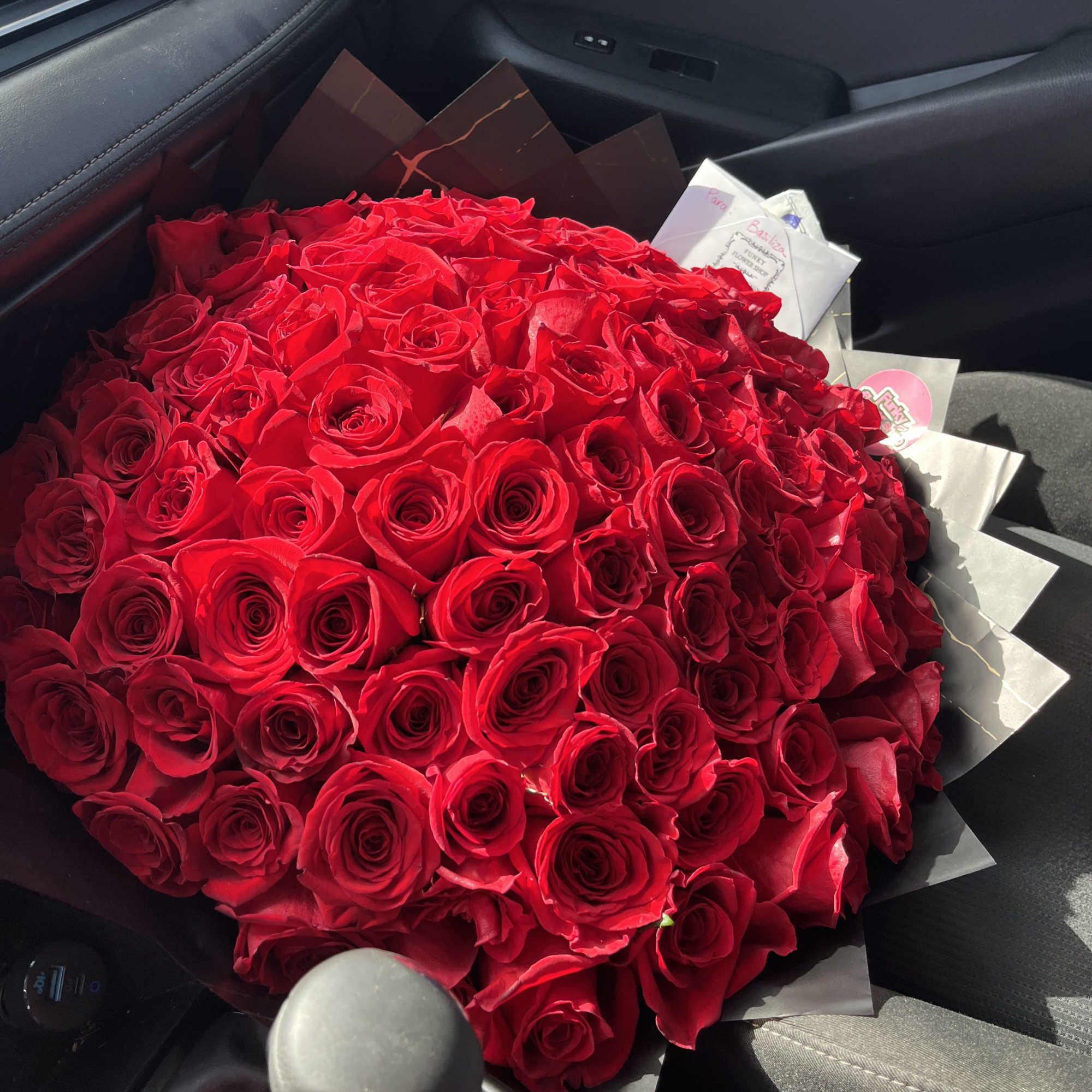 Large bouquet of red roses wrapped in dark paper on a car seat