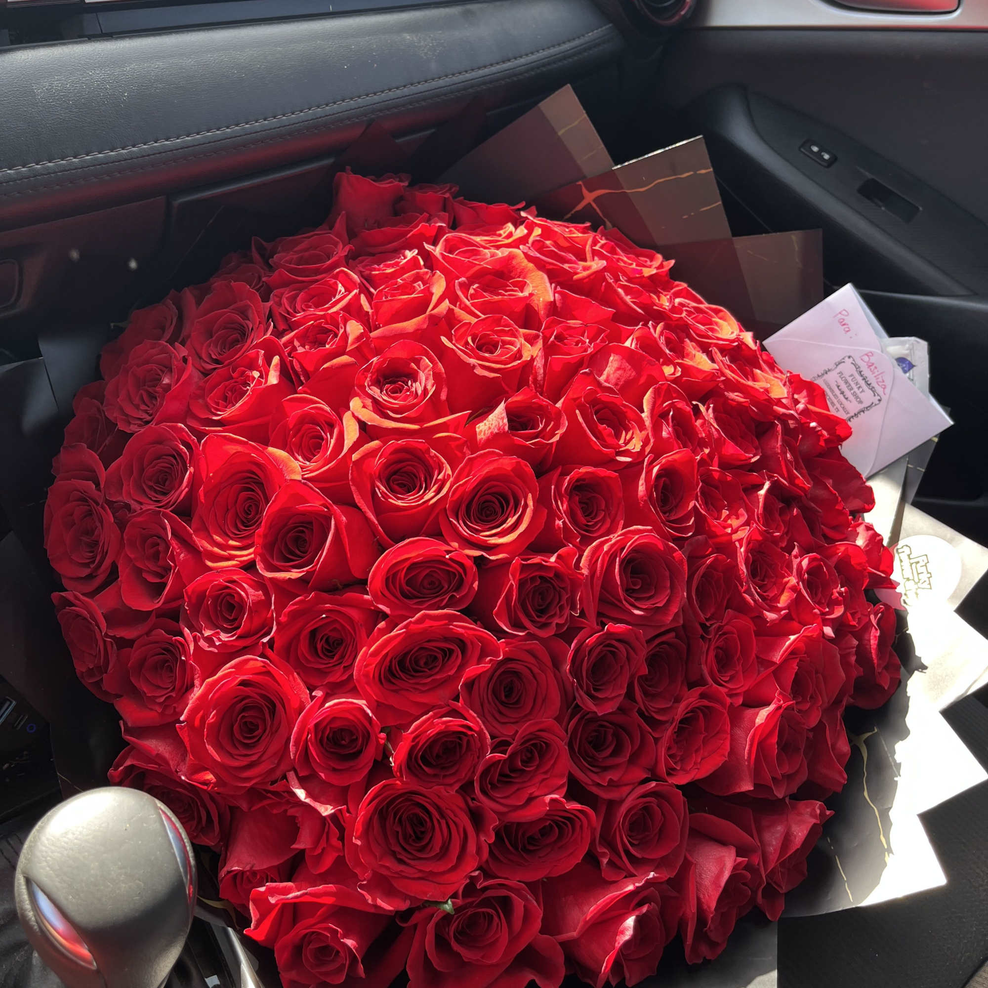 Large bouquet of red roses wrapped in black paper on a car seat