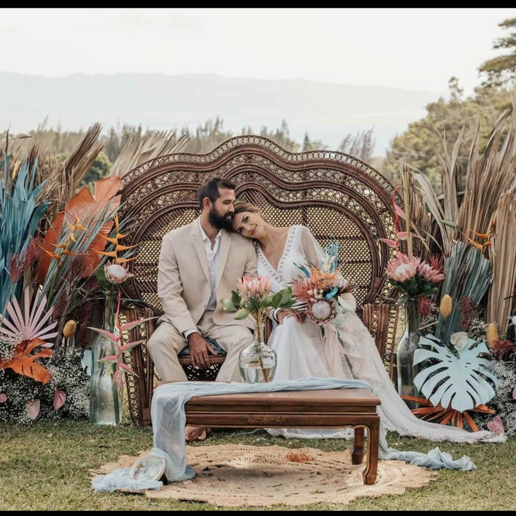 Couple seated on an ornate outdoor wedding backdrop with tropical floral decor