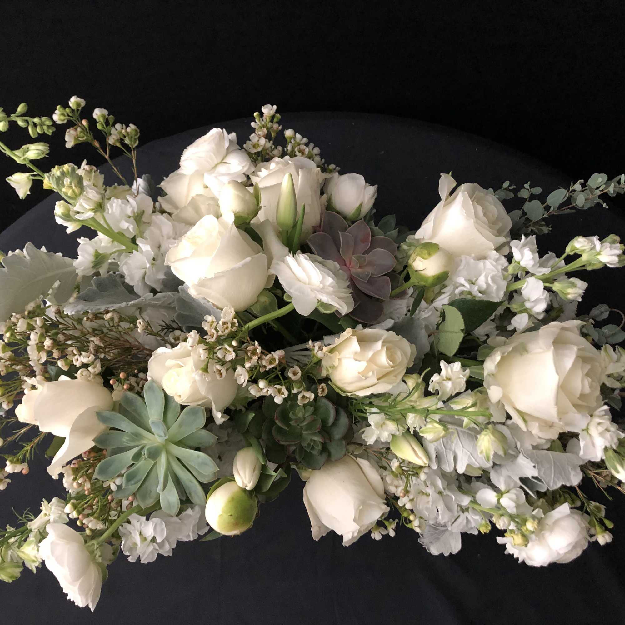 Low arrangement of white roses and small white flowers with succulents