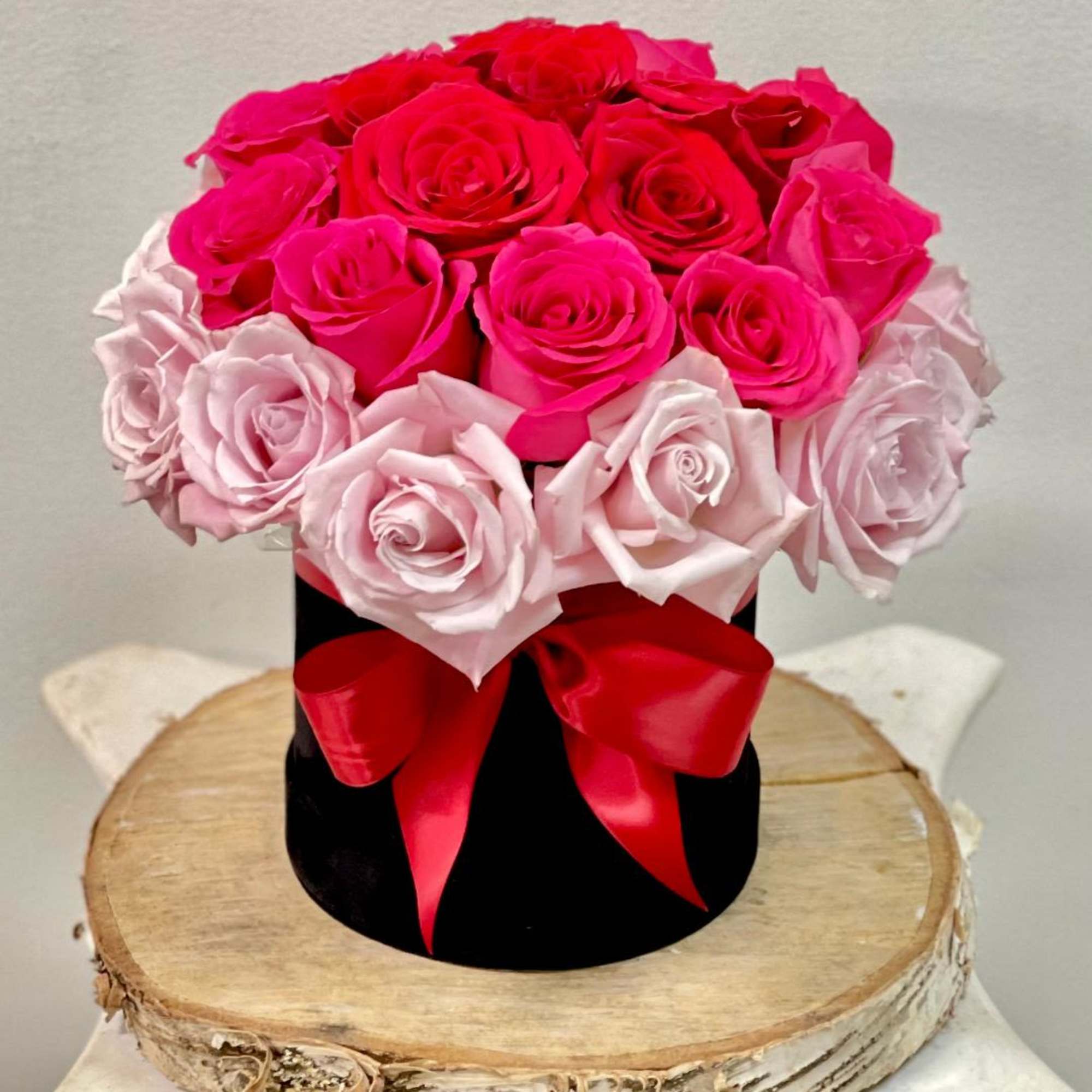 Pink and red roses arranged in a black hat box with a red ribbon