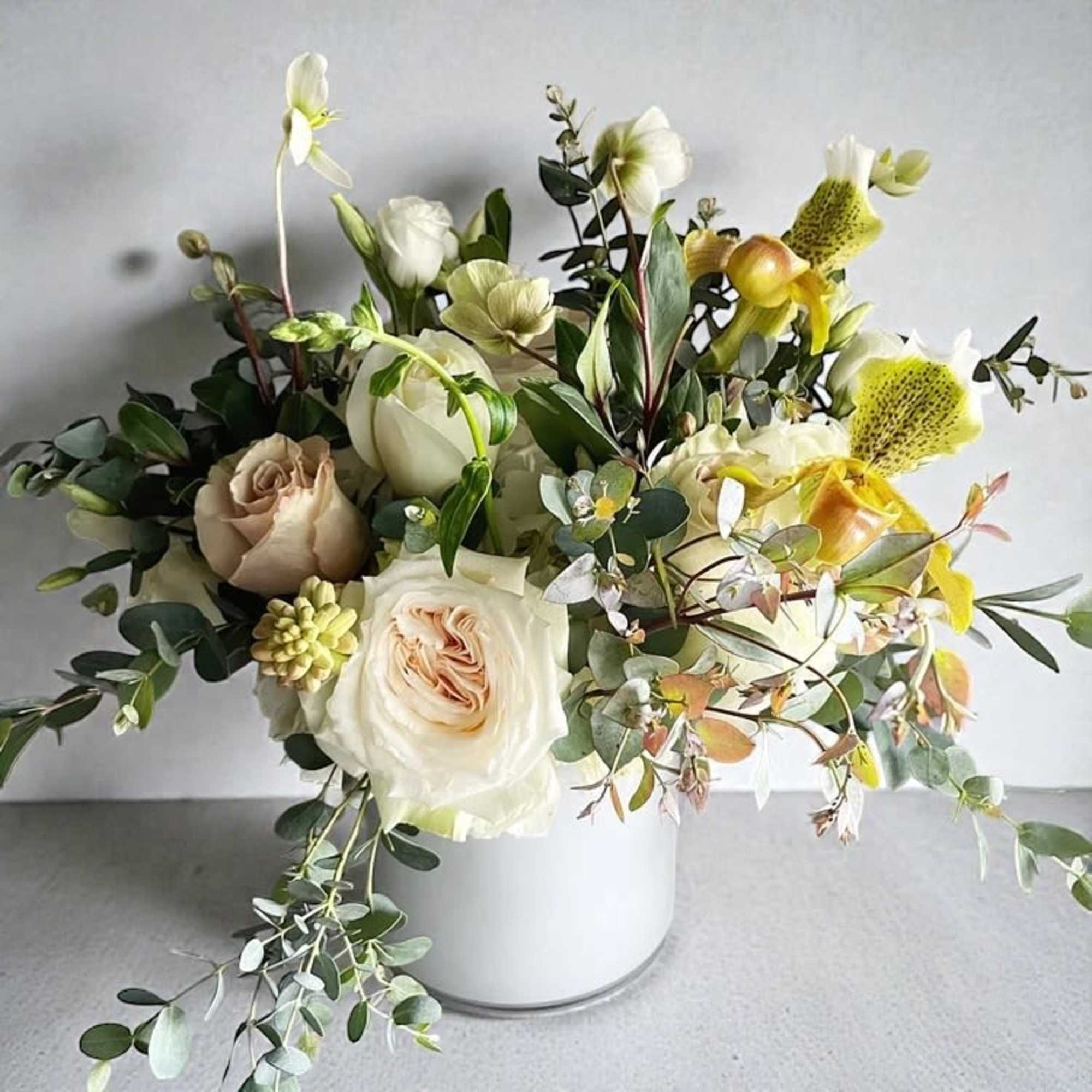 Cream and pale peach flower arrangement with roses and orchids in a white cylinder vase