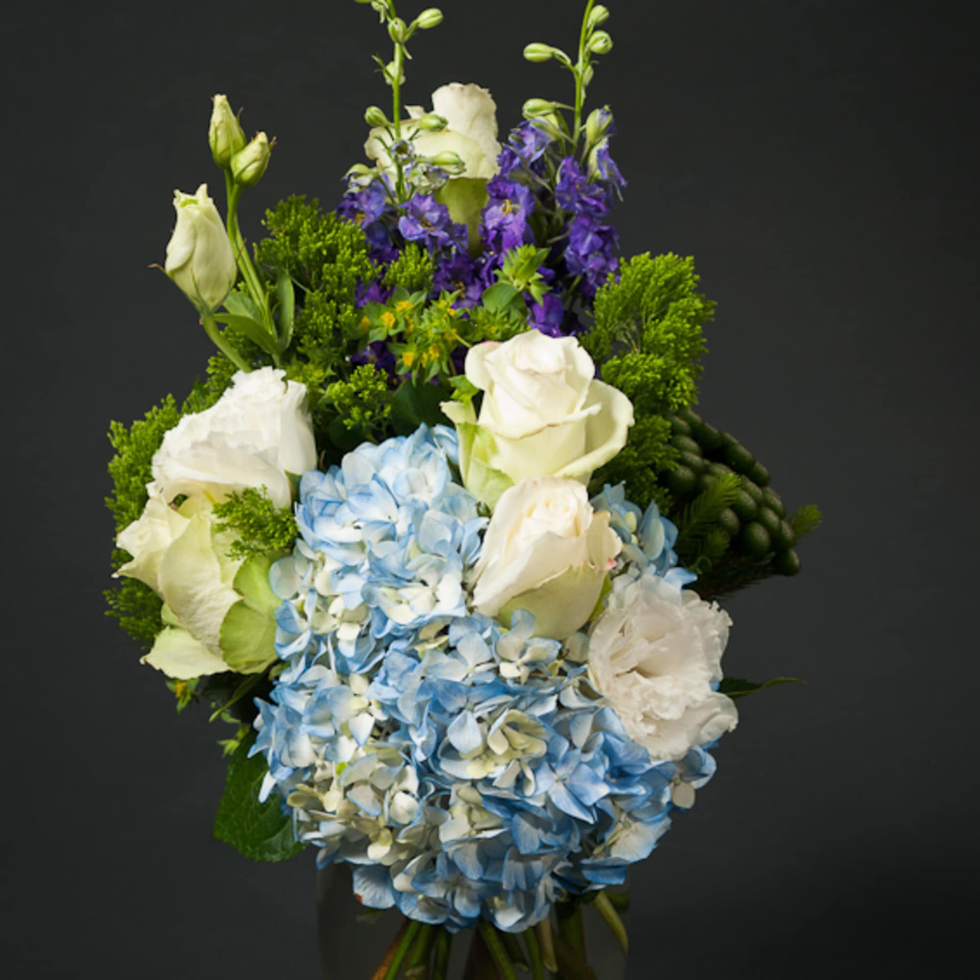 Blue hydrangeas and white roses in a glass vase with purple flowers