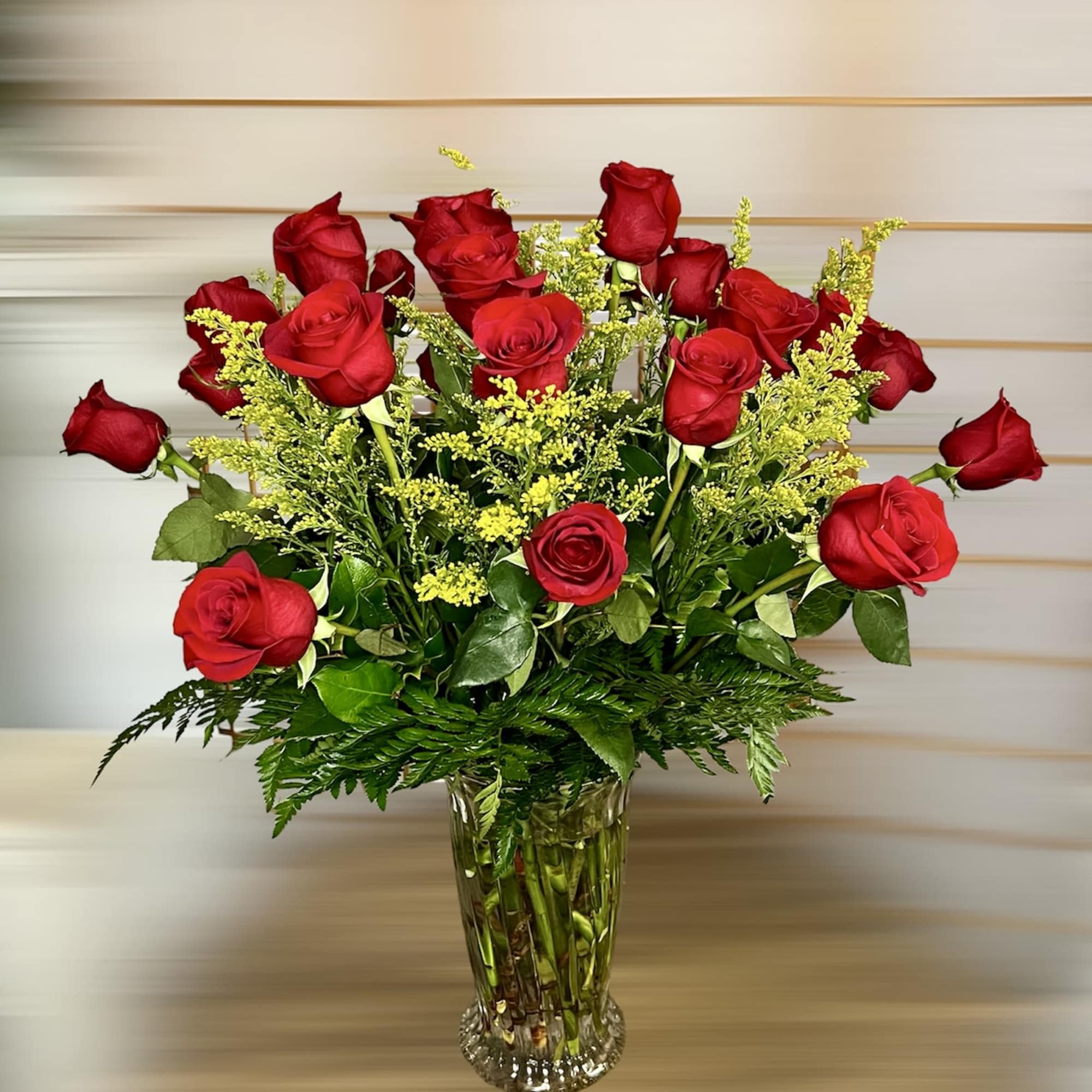 Red roses arranged in a clear glass vase with yellow filler flowers