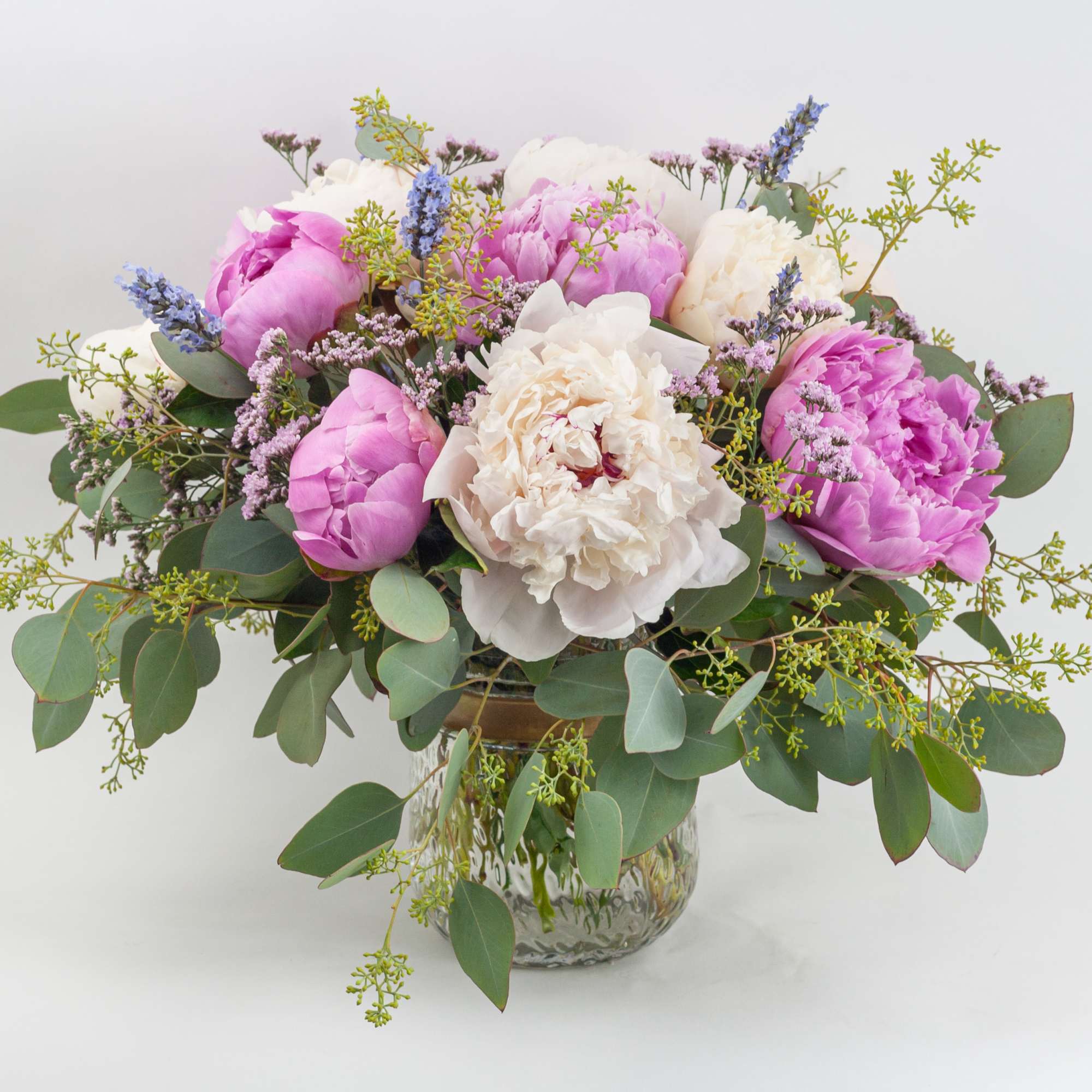 Low glass vase arrangement with pink and white blossoms and purple accents in a loose, full design