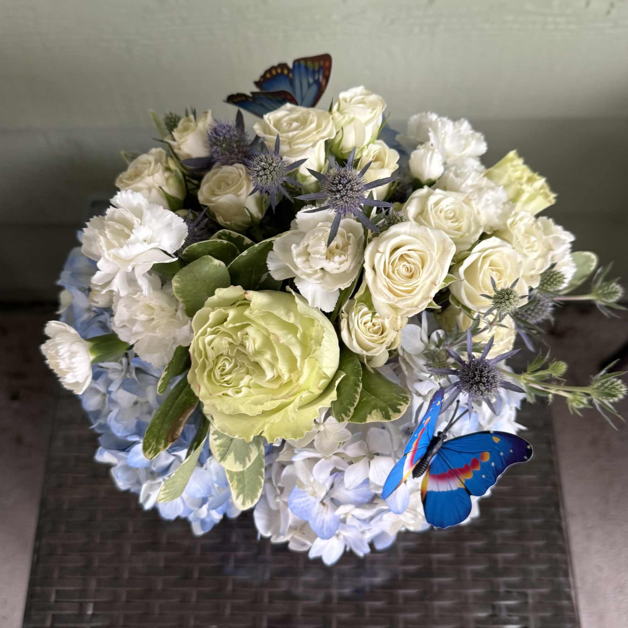 Bouquet of cream roses, white carnations, and blue hydrangeas with butterfly accents