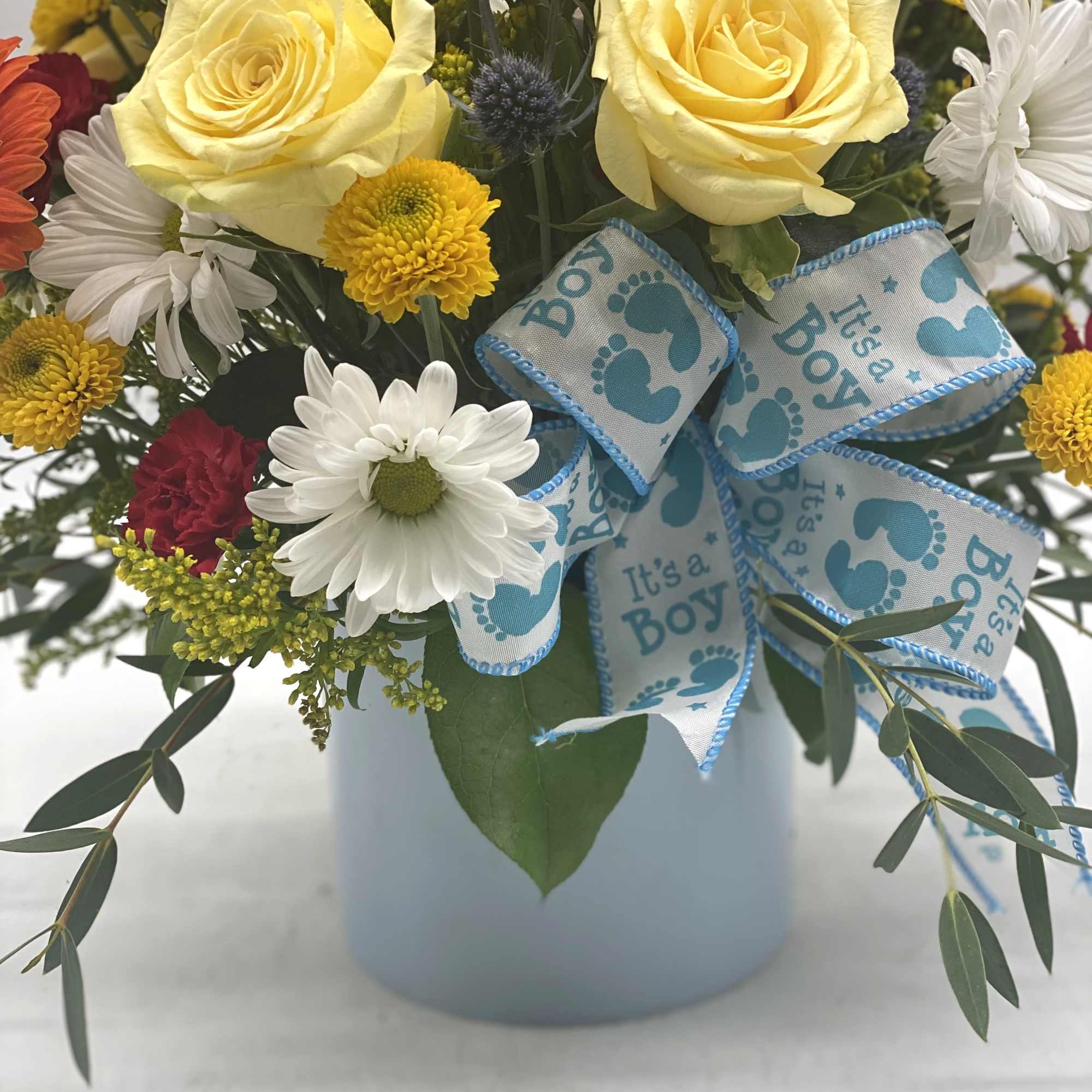 Bouquet of yellow roses and daisies with a blue "It's a Boy" ribbon in a white vase
