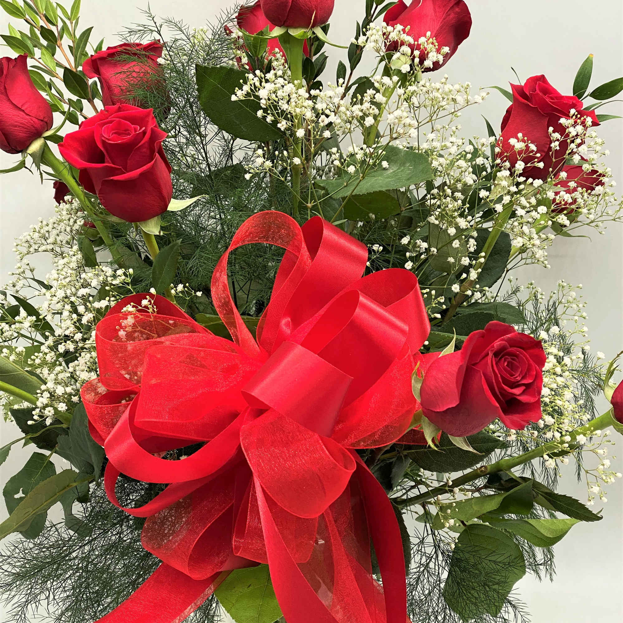 Red roses with baby's breath and a large red bow in a glass vase
