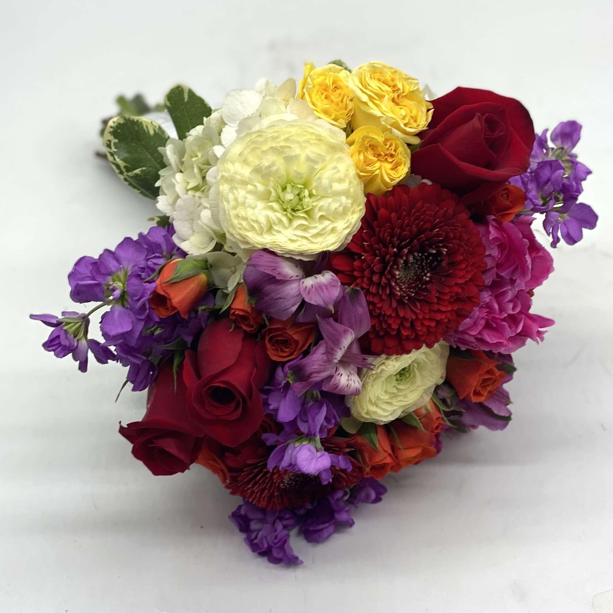 A lush mix of red roses, pale yellow ranunculus, red gerbera daisies