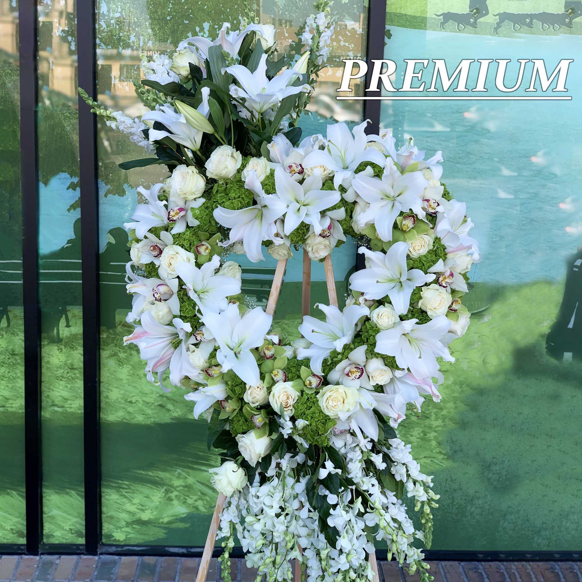 Heart-shaped white lily and rose wreath with trailing blooms on a wooden easel stand