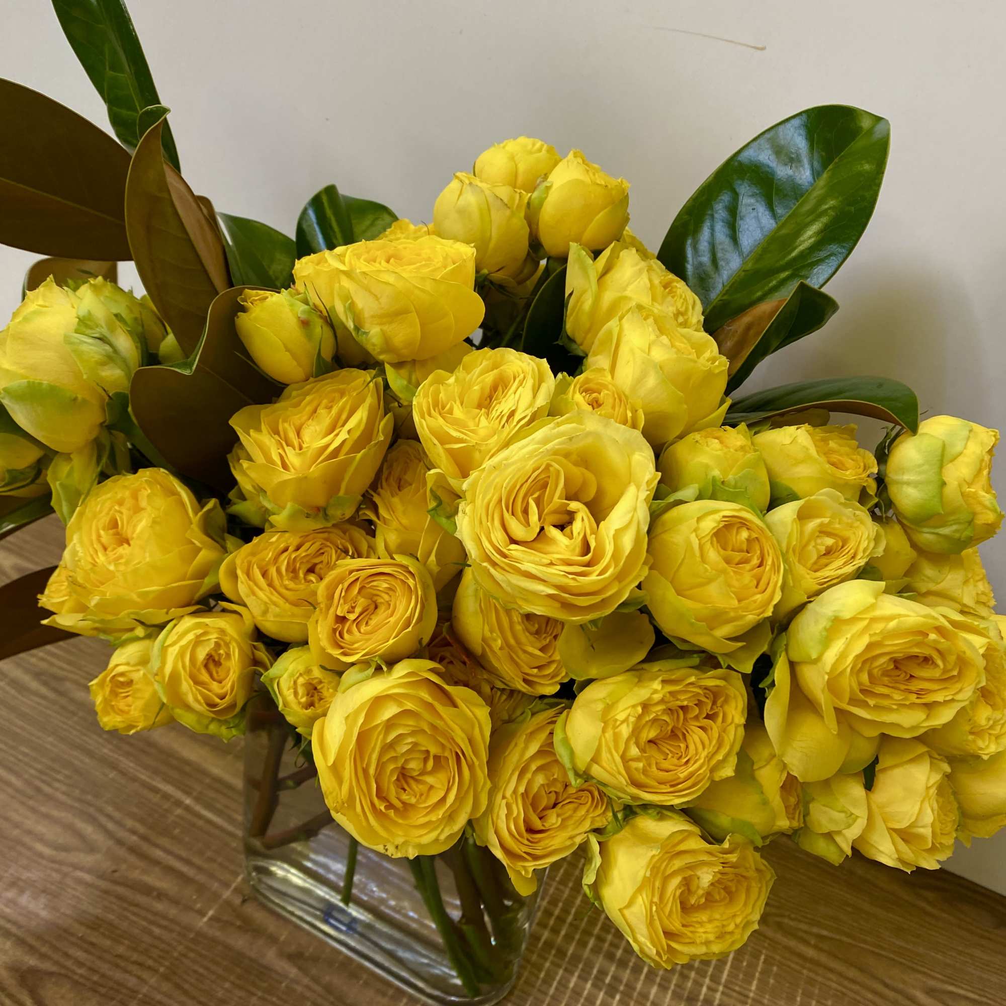 Yellow roses arranged in a clear glass vase with glossy leaves