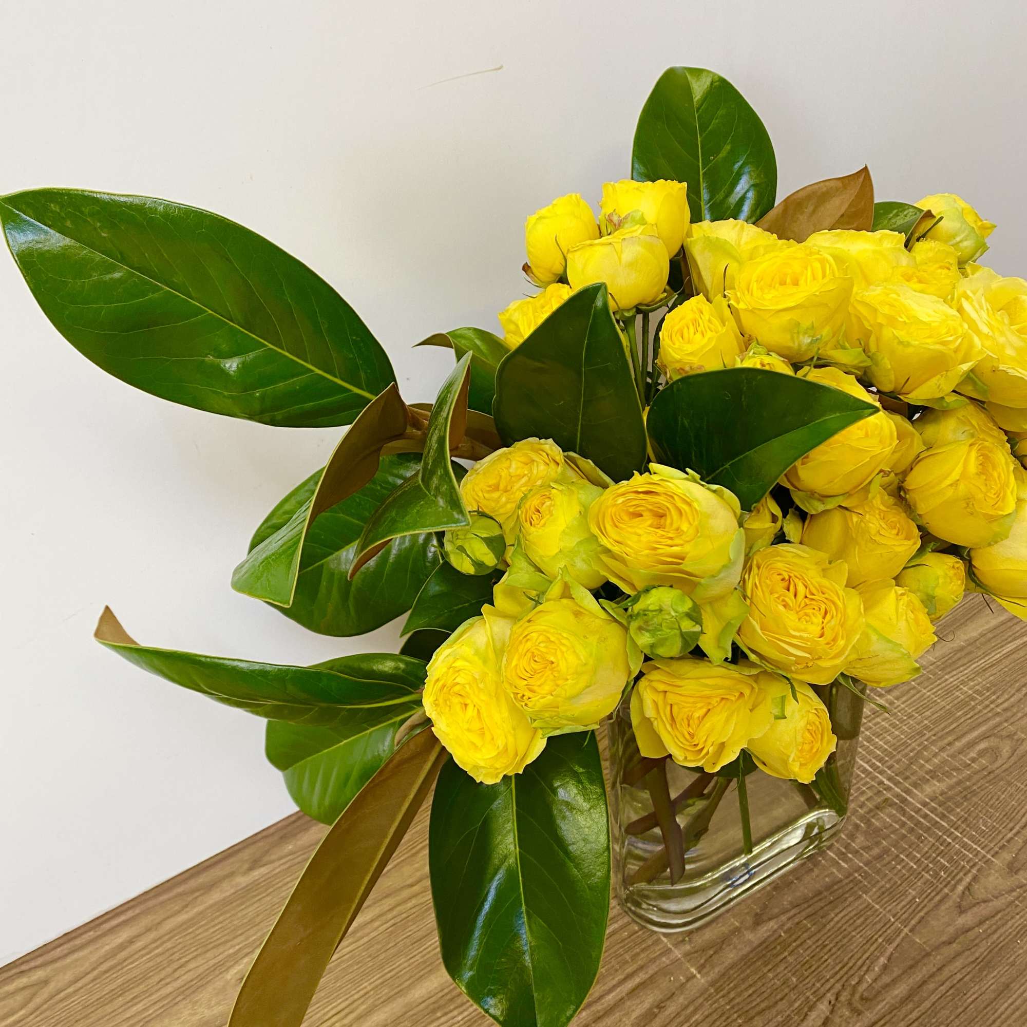 Yellow roses arranged in a clear glass vase with large glossy leaves