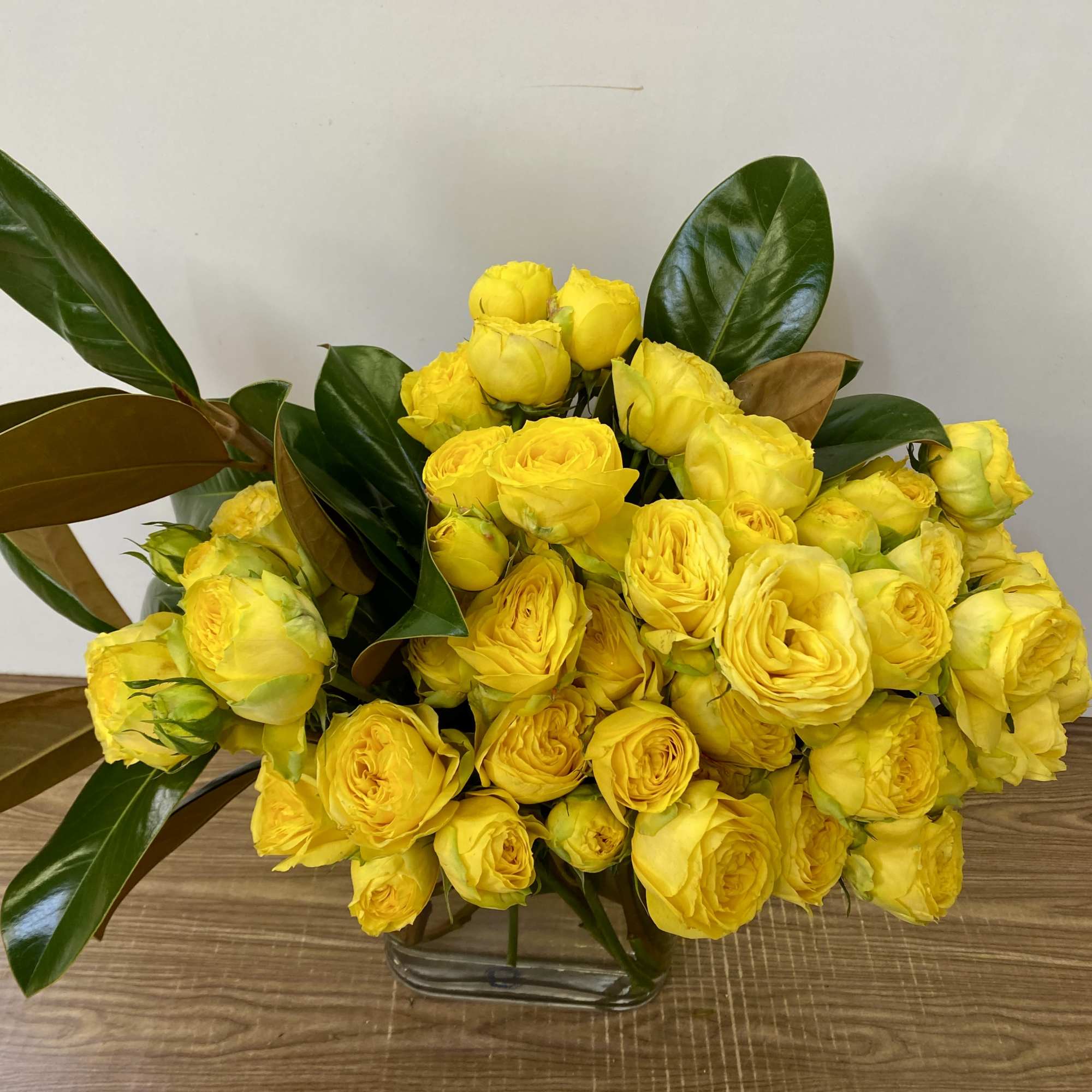 Yellow rose bouquet in a clear glass vase with large glossy leaves