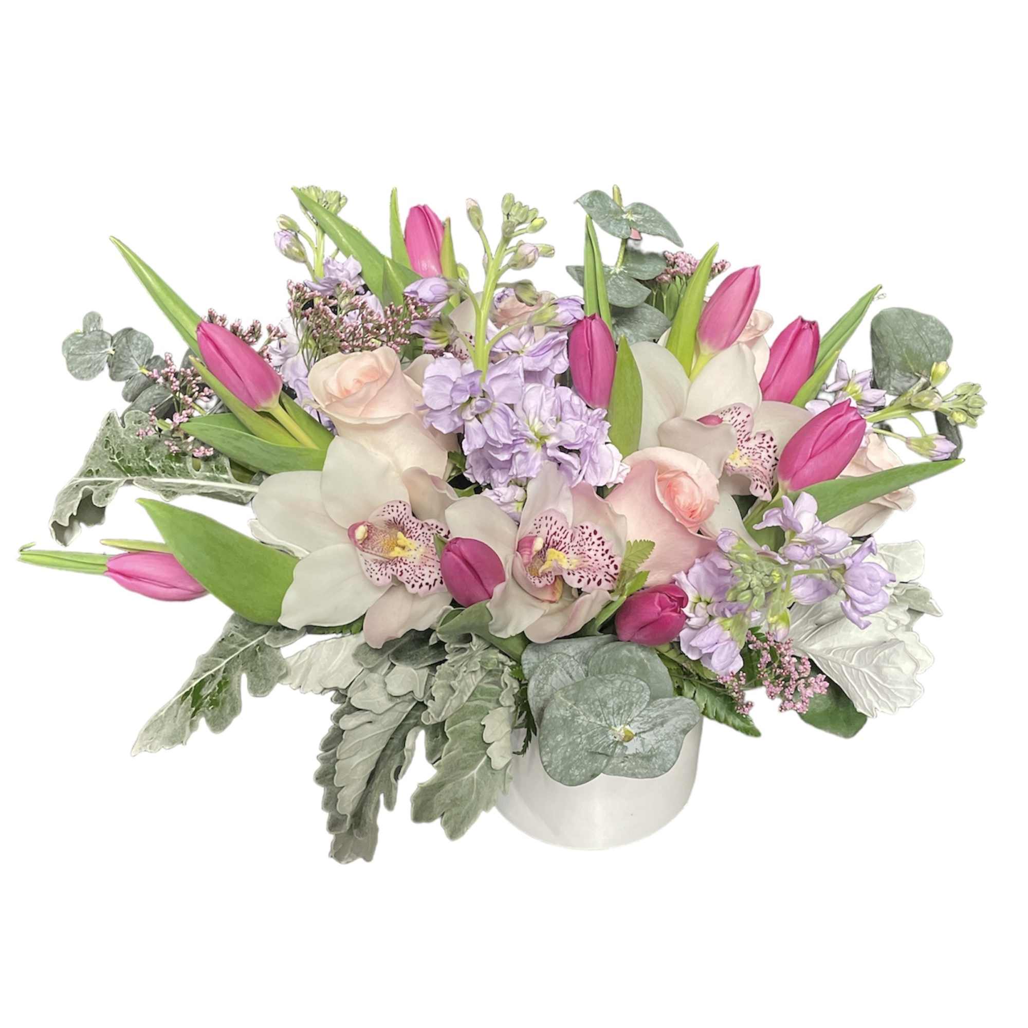 Low arrangement of pink tulips, blush roses, orchids and lavender flowers in a white vase.