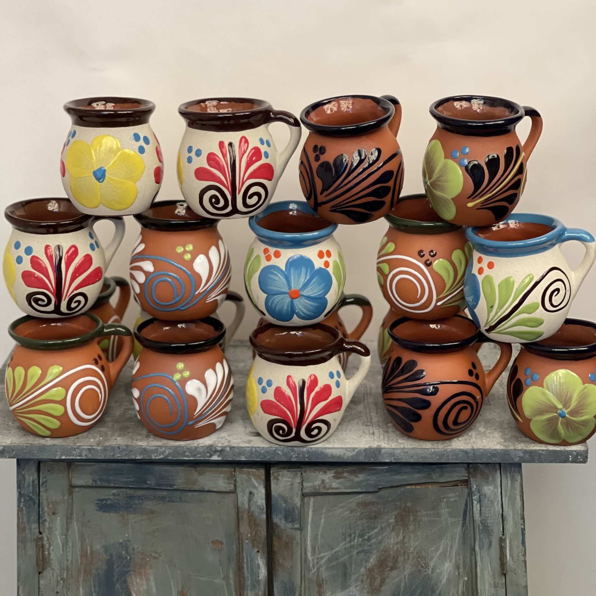 Stacked painted ceramic mugs with colorful floral designs