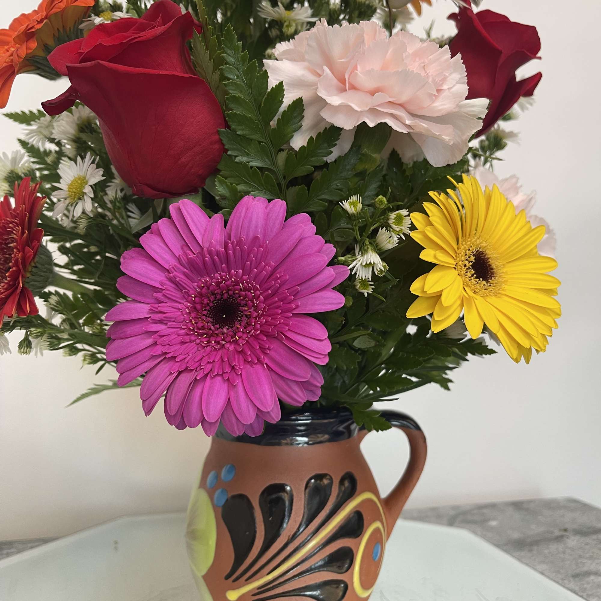 Mixed bouquet in a painted ceramic mug vase with bright gerberas and roses