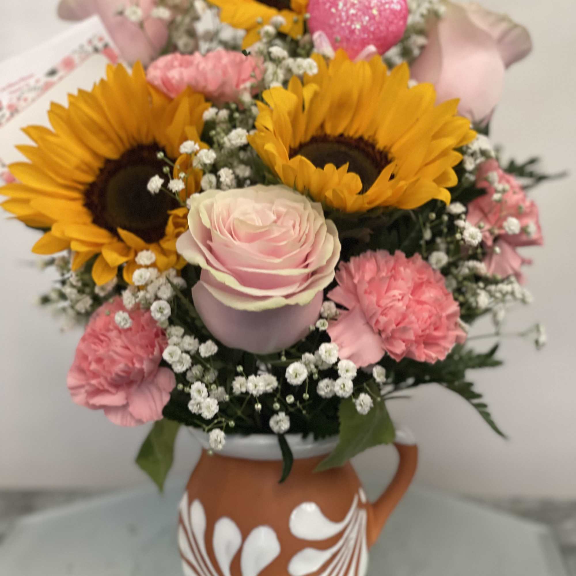 Bouquet of sunflowers, pink roses, and carnations in a painted ceramic pitcher