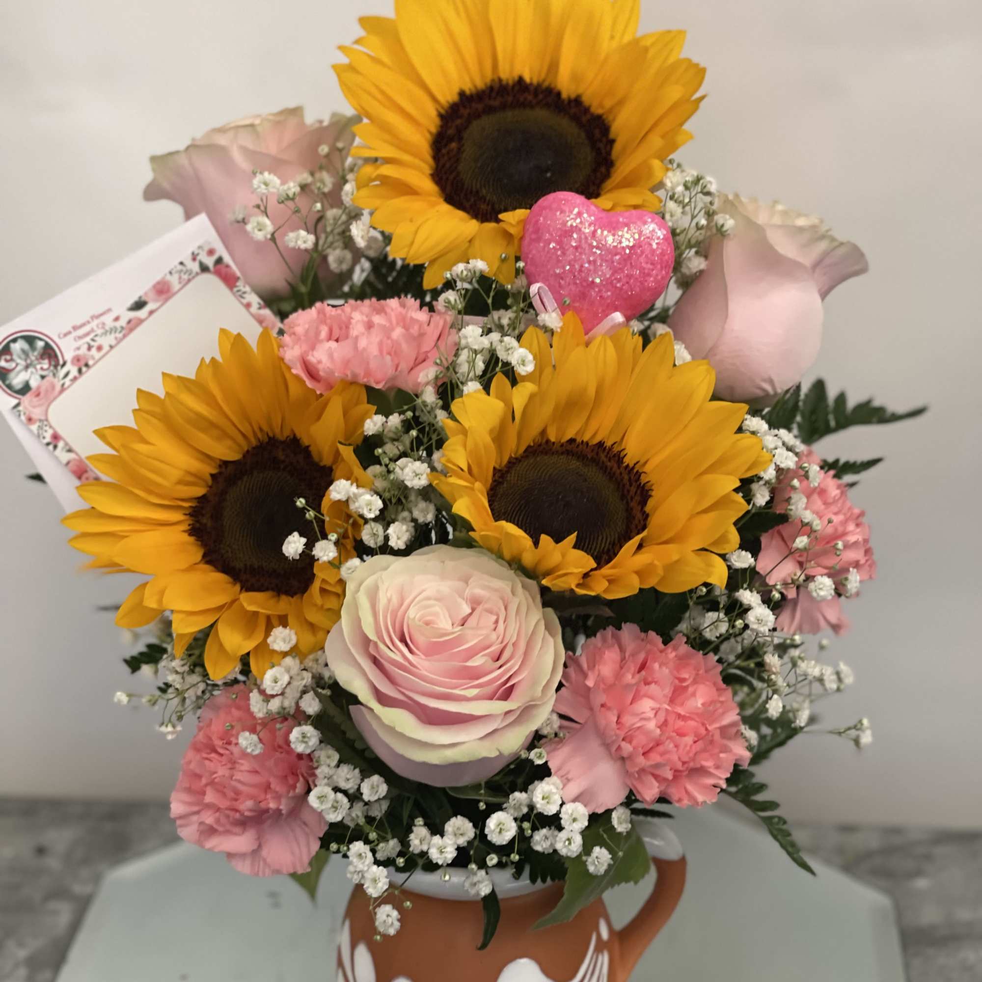 Sunflower and pink rose bouquet in a decorative mug with a pink heart pick