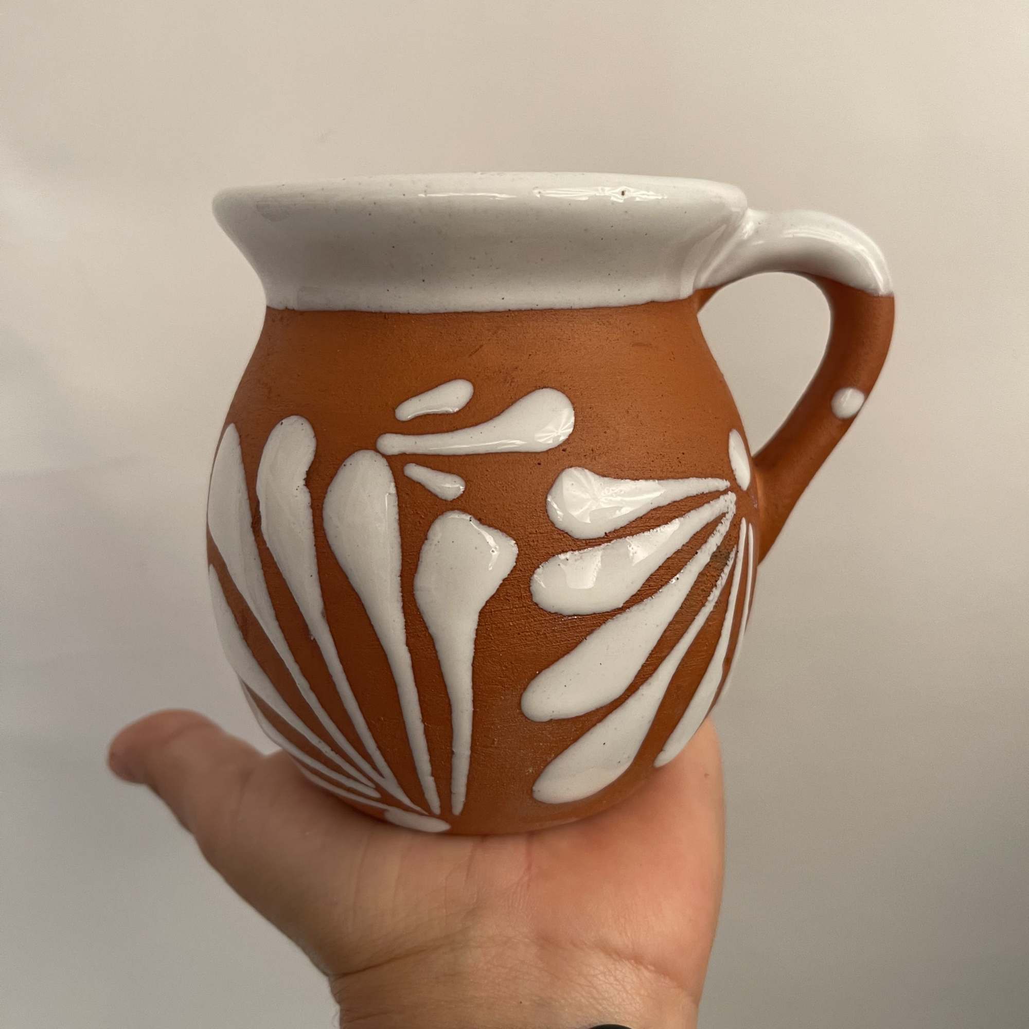 Small terracotta ceramic pitcher with white painted leaf design