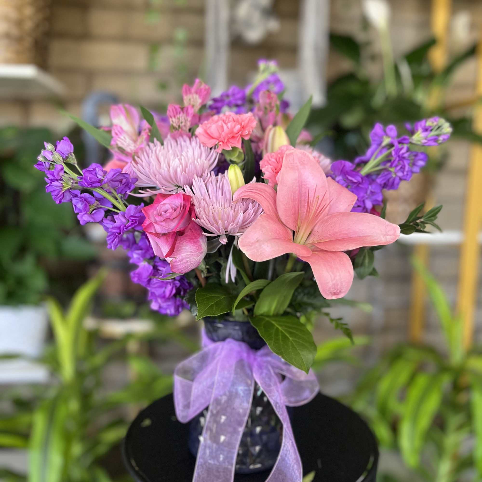 Pink and purple mixed bouquet in a dark vase with a lavender ribbon